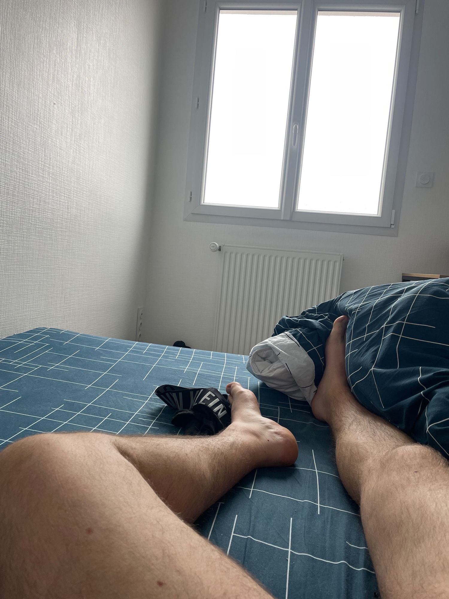 Je suis allongé nu sur mon lit. Cuisses et jambes poilues apparentes. Boxer de marque CK déposé auprès de mon pied gauche. La fenêtre en arrière plan laisse apparaitre un temps sombre et maussade.