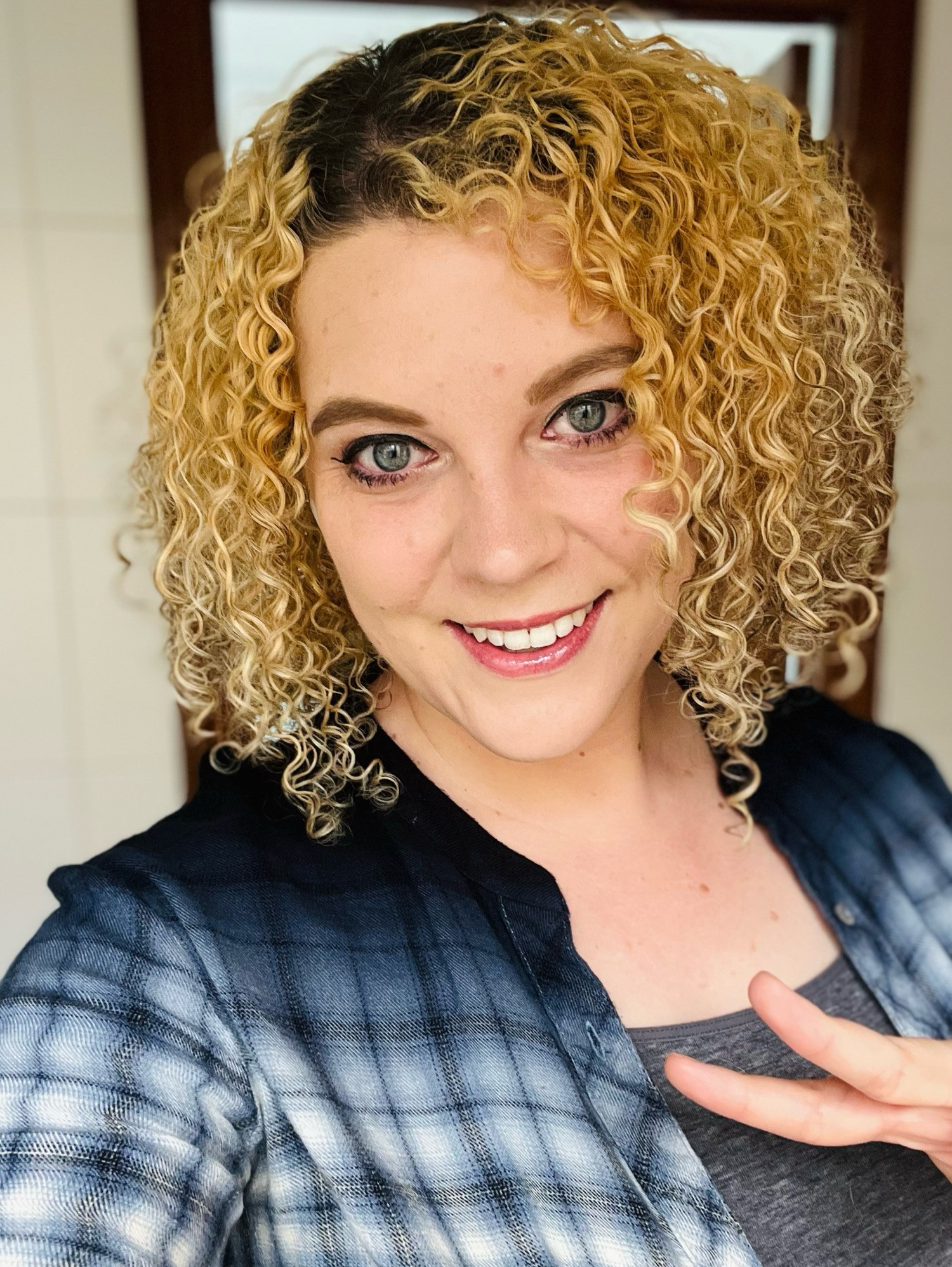 Selfie of Emily smiling, wearing a blue and gray plaid shirt and generally looking very happy