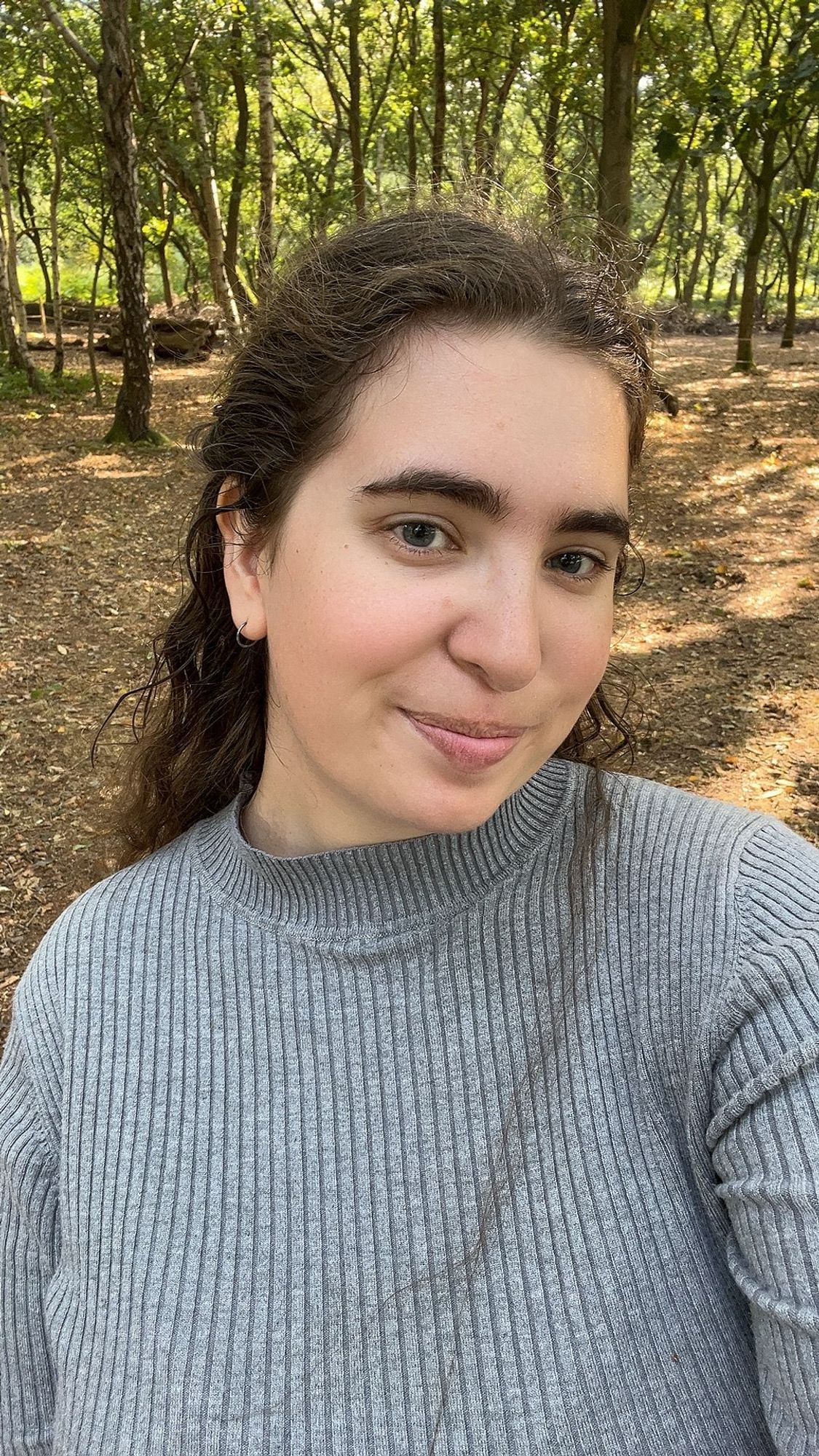 Stephanie Black, standing amongst trees, smiling at the camera.