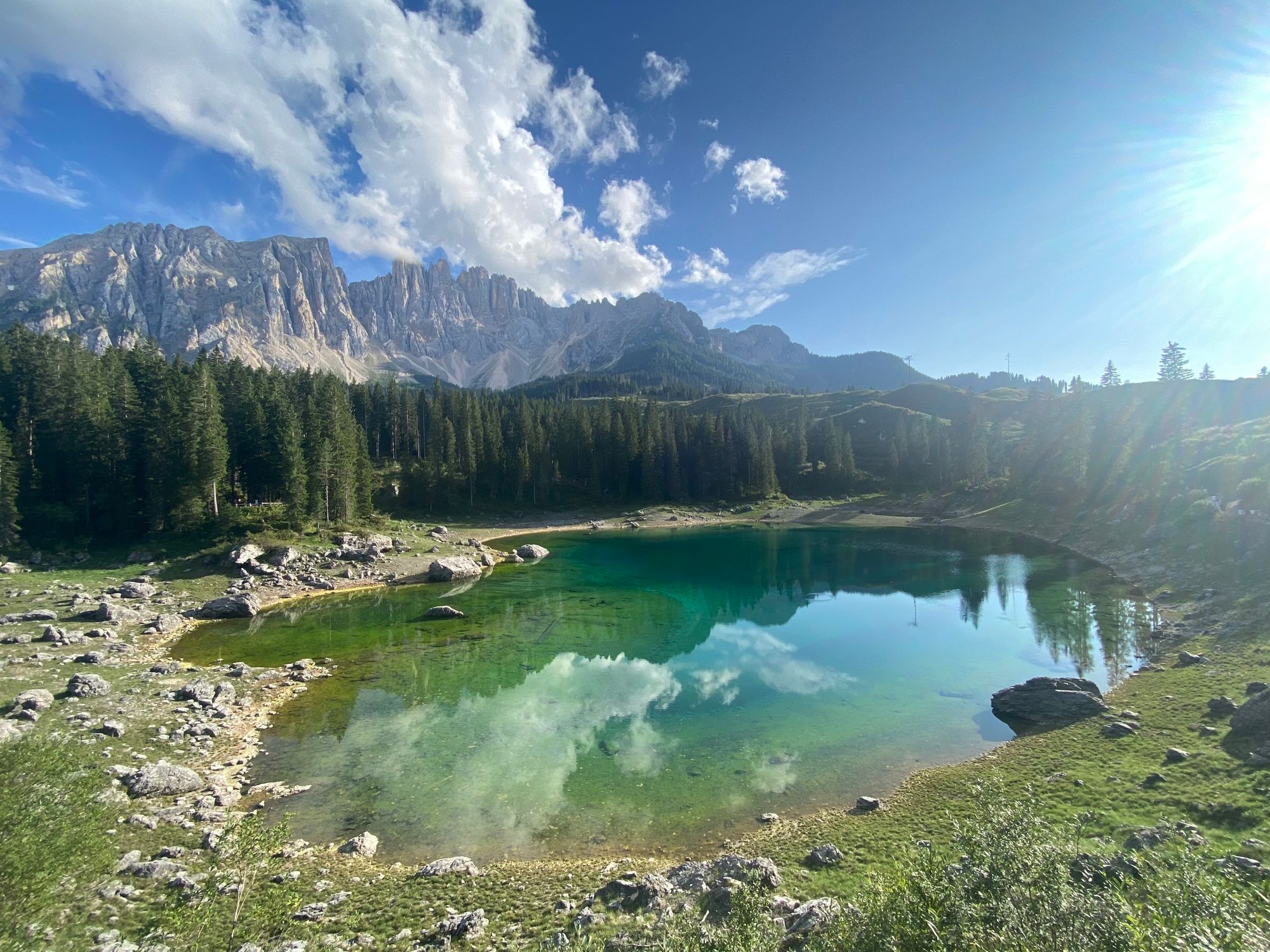 Carezza lake reflecting a bit cloudy sky and par of the Latemar summits