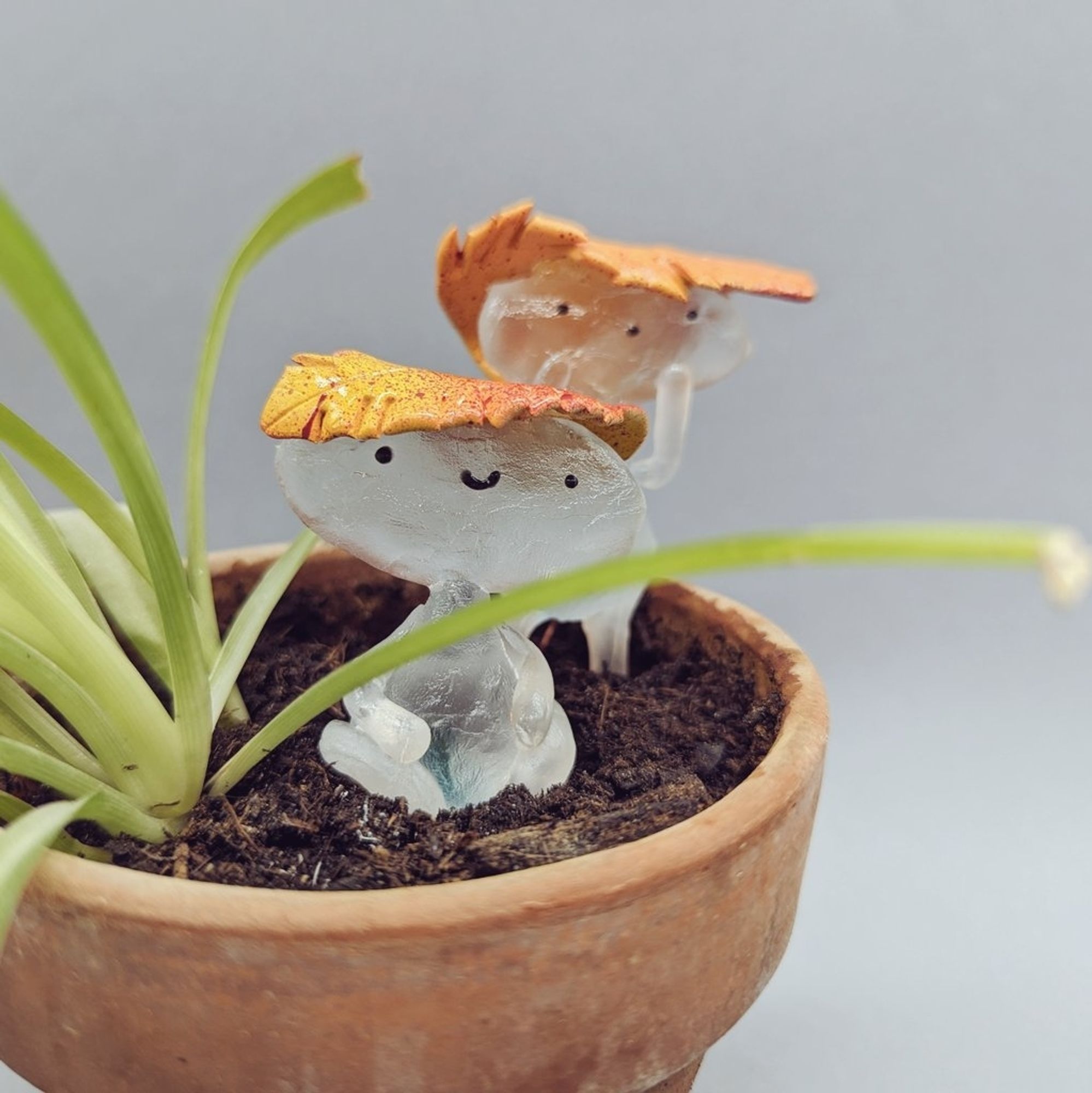 Petit bonhomme en verre avec une feuille morte en chapeaux fait en résine. Il est dans un pot de fleurs