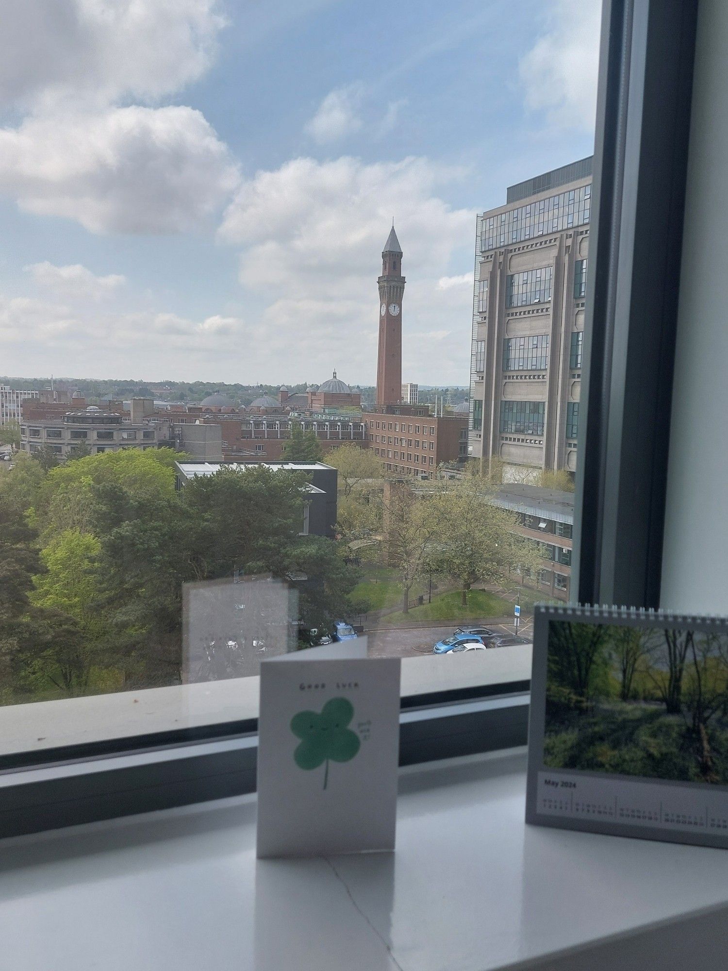 View from an office window showing the Birmingham University clock tower and on the windowsill is a calendar open on May and a good luck card