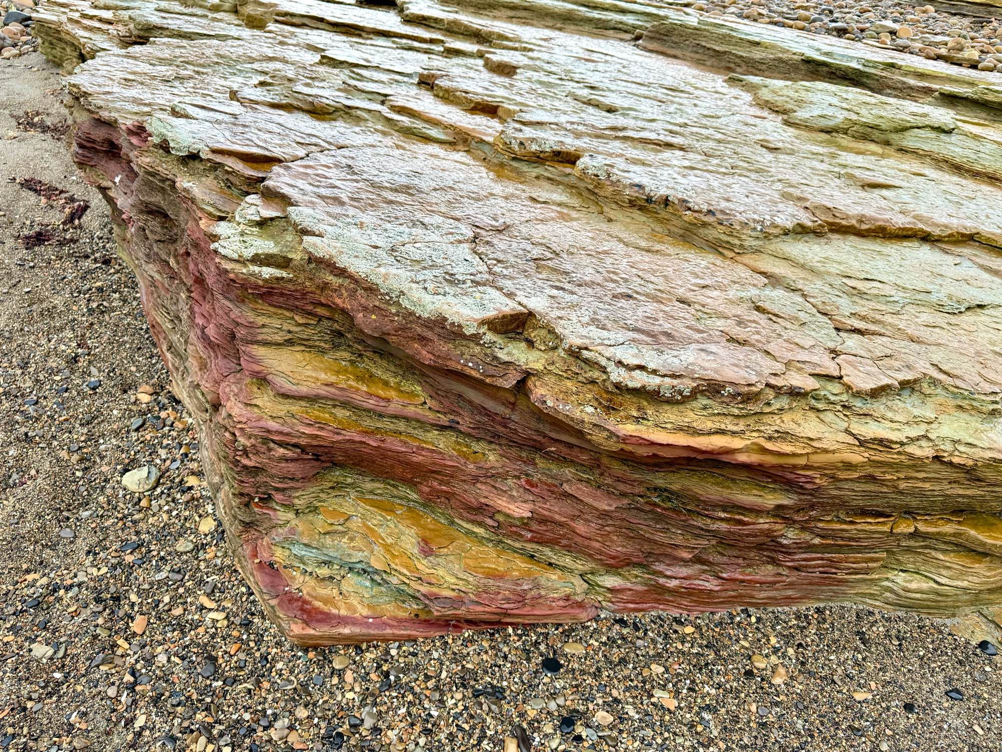 striated rock on sole shingley sand showing stripes of red, orange, green