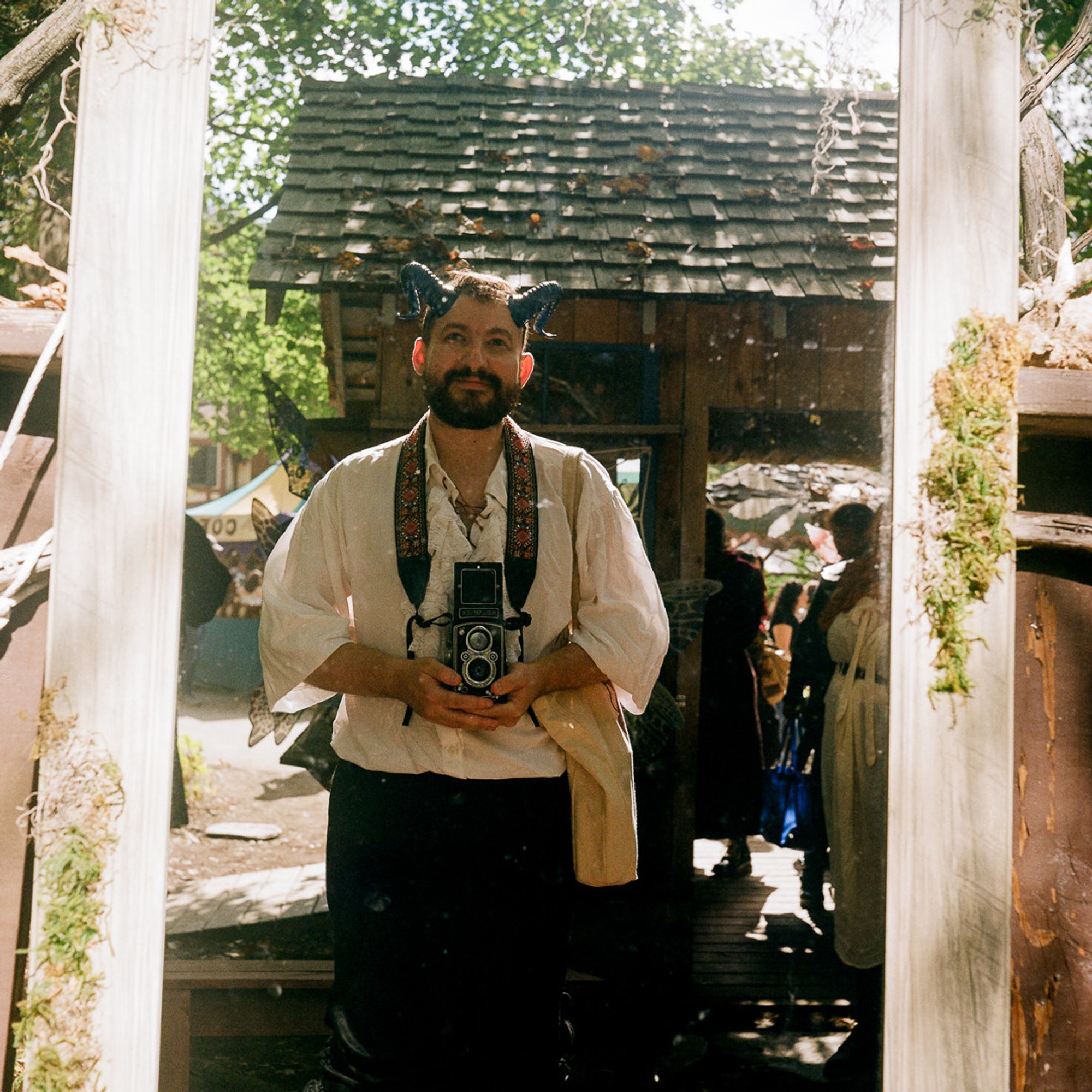 a self portrait of a smiling man, dressed up for a renaissance faire with, holding a rolleiflex camera