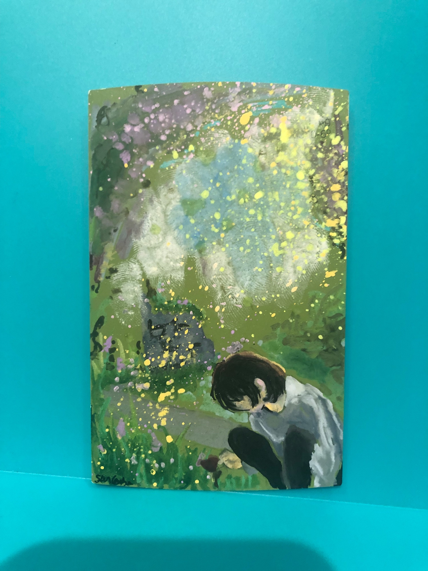 A drawing on a green paint chip. It’s a drawing of a man crouched in a garden, looking at flowers. The center of the piece gets lighters, and is more white/blue, wear the rest is overwhelmingly green, with paint splatters throughout to look like flowers. 