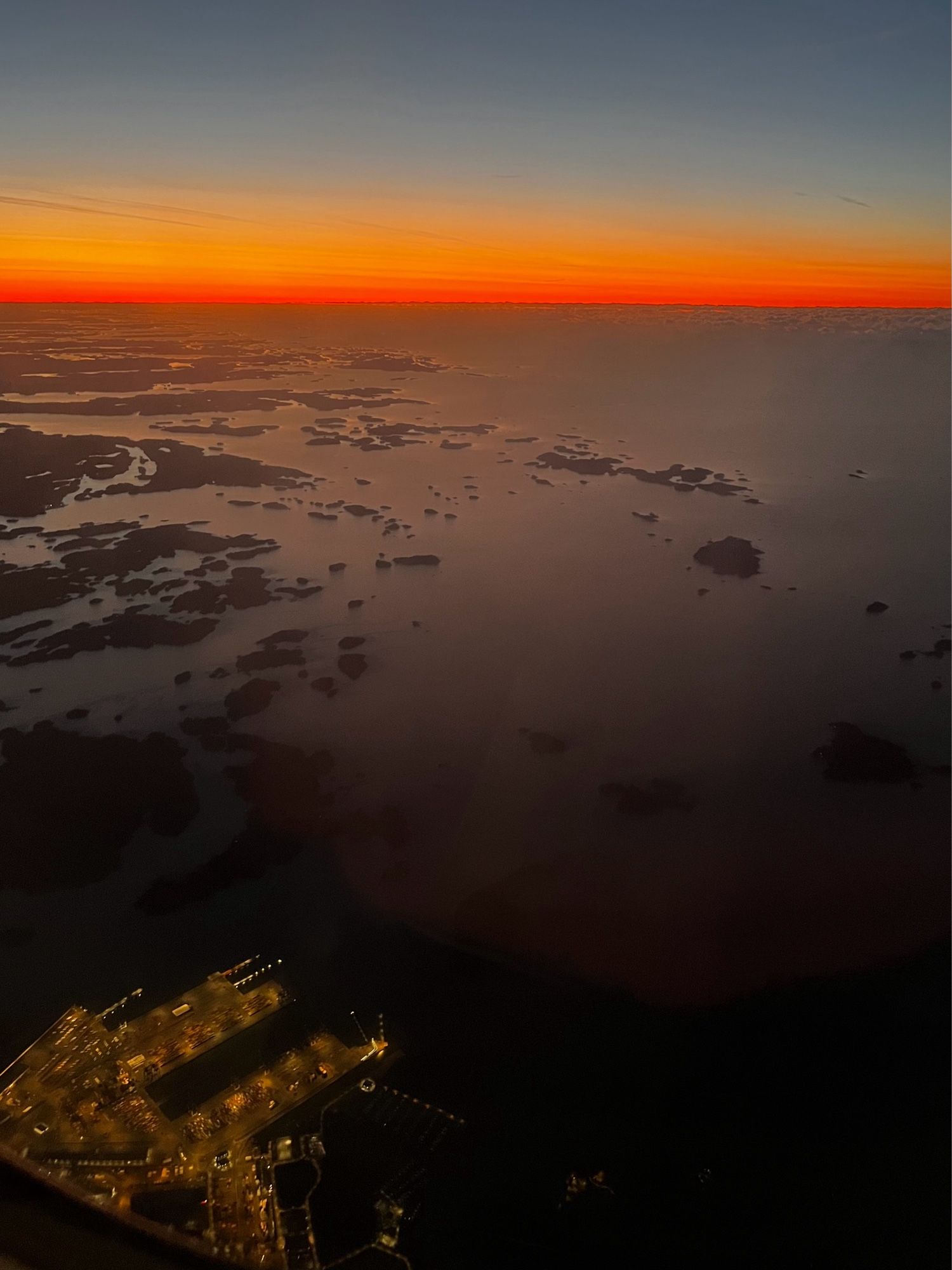 Vähän nousun jälkeen klo 6am otettu kuva, missä näkyy oranssi taivaanranta ja Vuosaaren satama