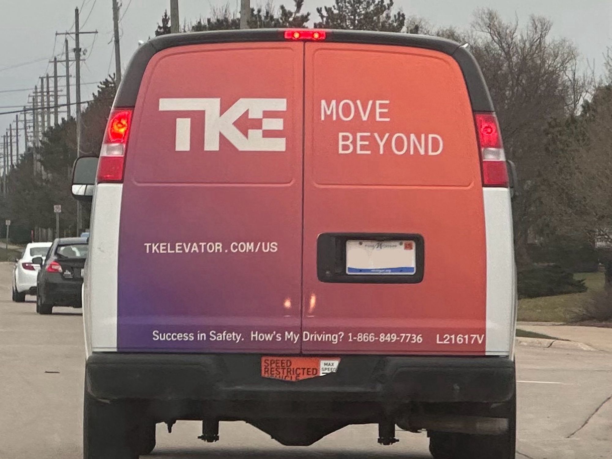 Photo of the back of a commercial van with a purple and salmon gradient wrap across the back with white marketing text. The relevant part of all this is that it’s for a company called T K Elevator with a logo made up of the three capital letters TKE. The middle section of the uppercase E is cut out so it forms an arrow with the uppercase K, pointing right to left as opposed to the left to right arrow found between the e and x in the FedEx logo…which is so specific it’s hard to see it as anything but a knock off that’s pointing backwards?