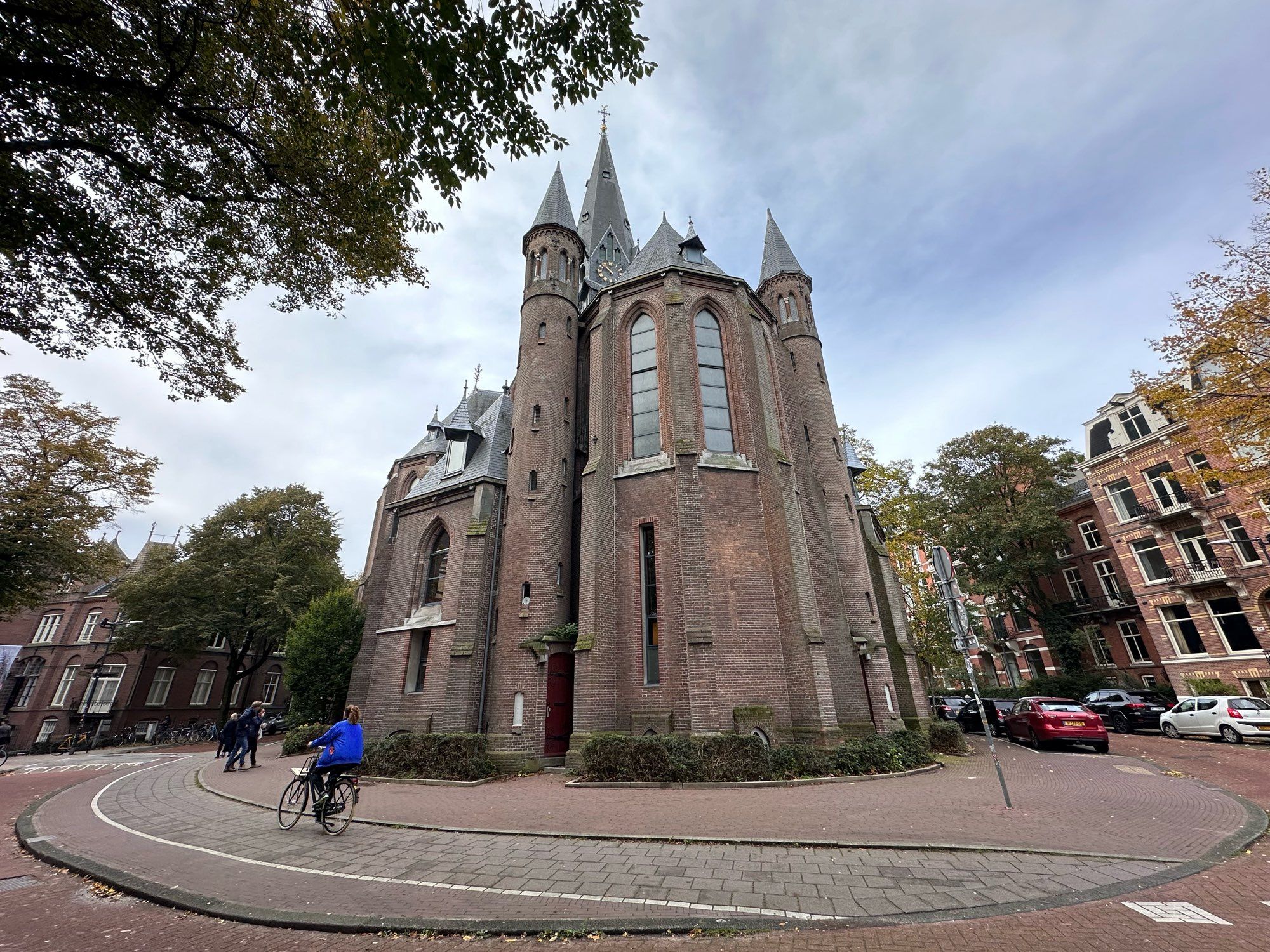 North side of Vondelkerk,looking up at the brick and stone church as a person wearing a blue jacket rides past.