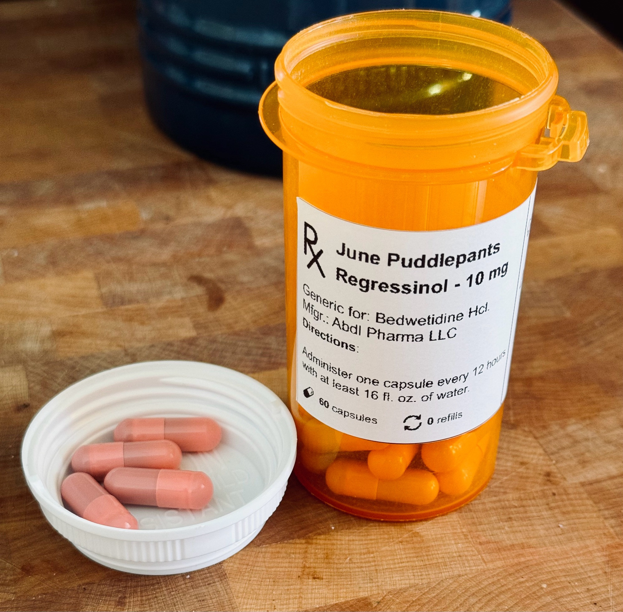 A prescription bottle with pink capsules in it and a fake label that reads:
June Puddlepants
Regressinol 10mg