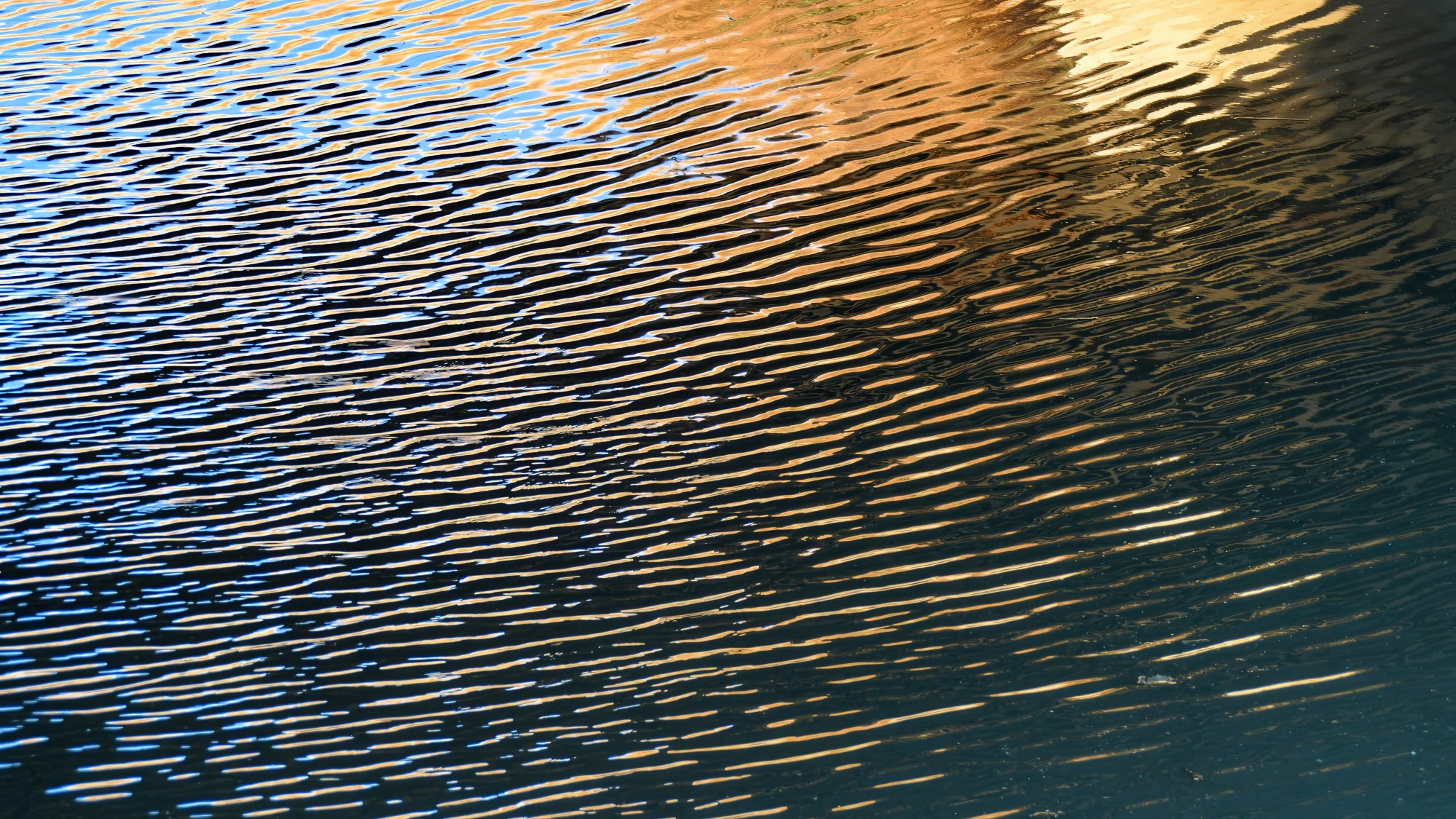 An abstract image of ripples in a creek, with reflections in various shades of blue, light brown and gray