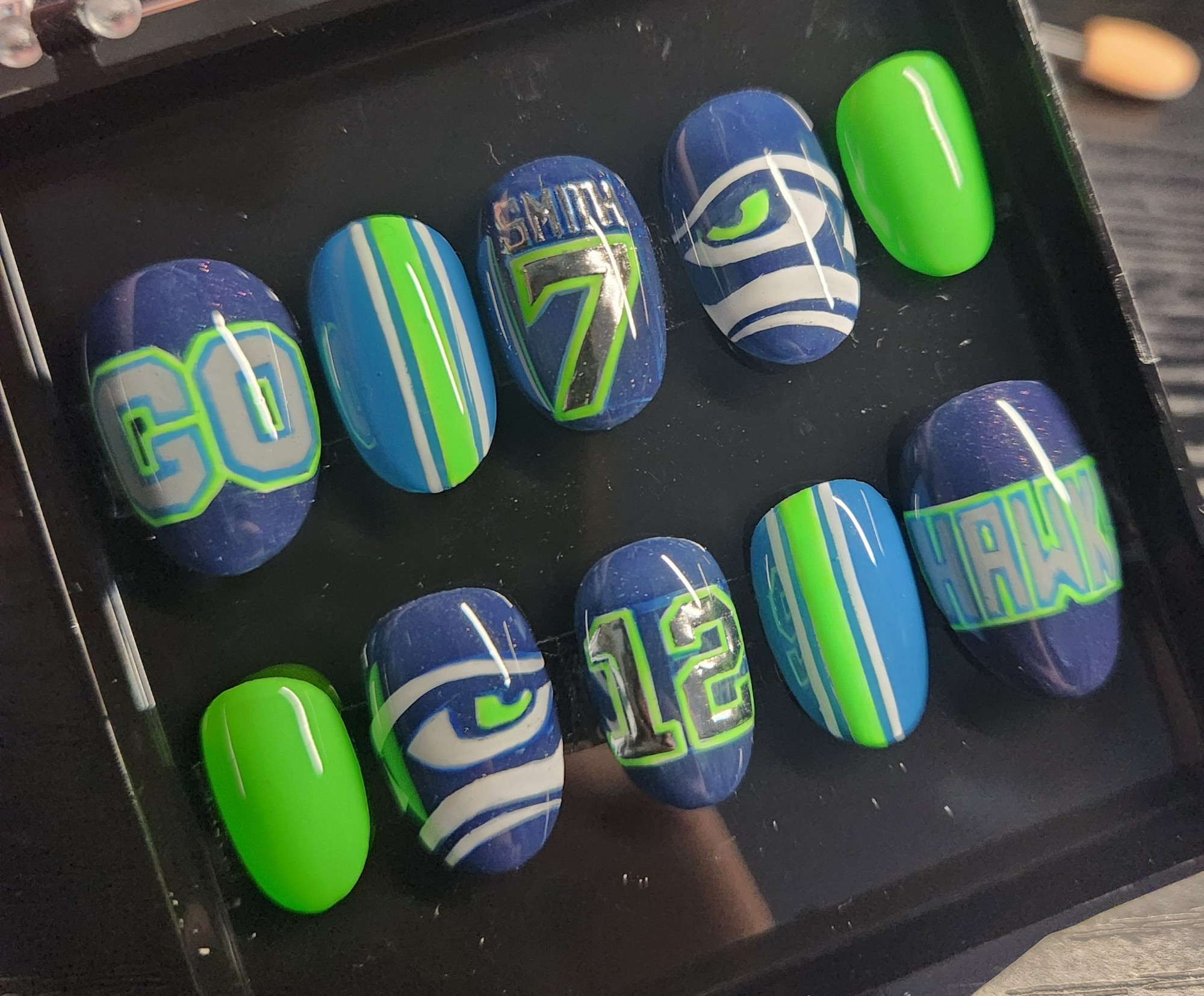 a set of short round press-on nails. they have Seahawks themed nail art, in navy blue, light blue, and neon green. 