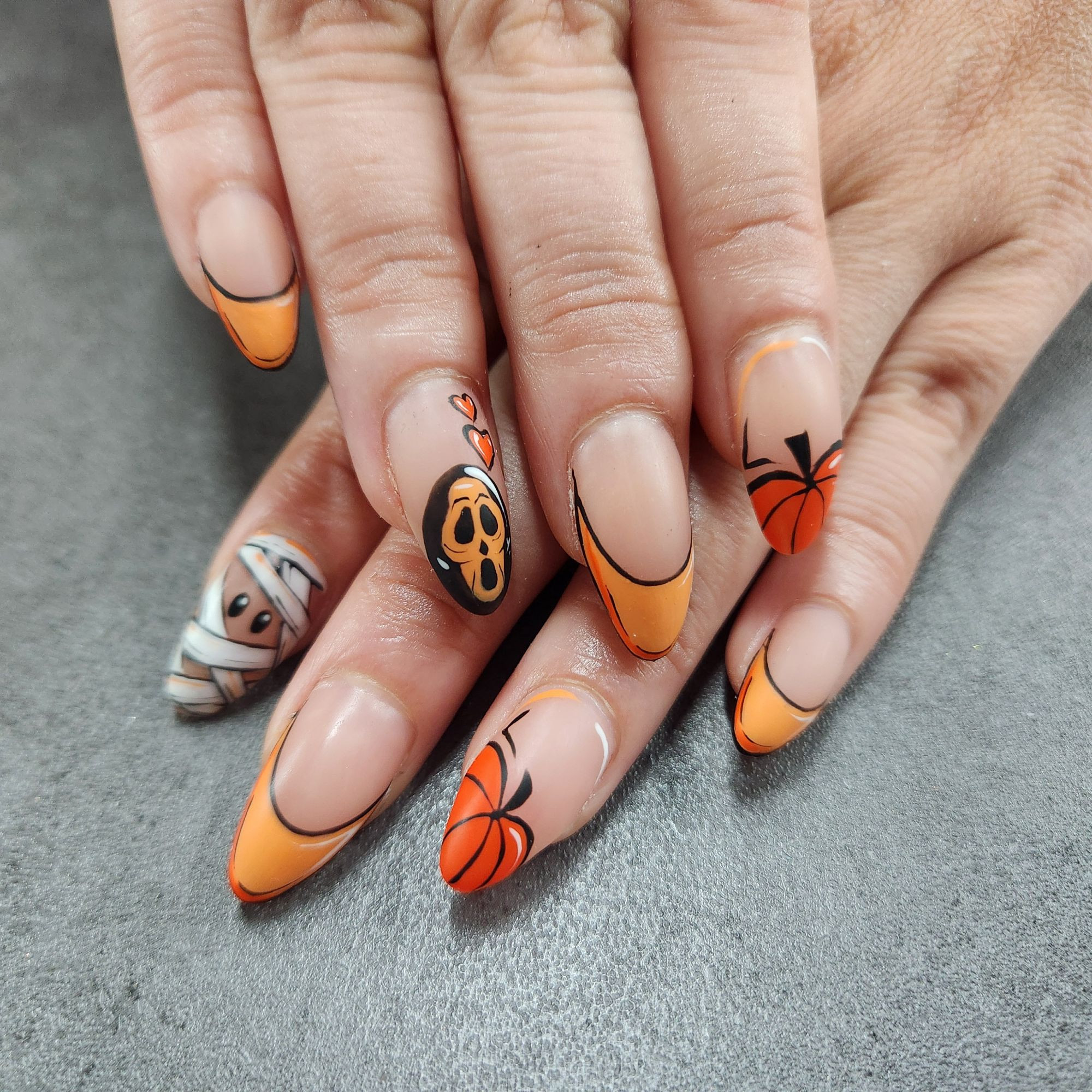 Picture of hands with almond shaped nails. Nail are matte, with pop art style Halloween designs in shades of orange.