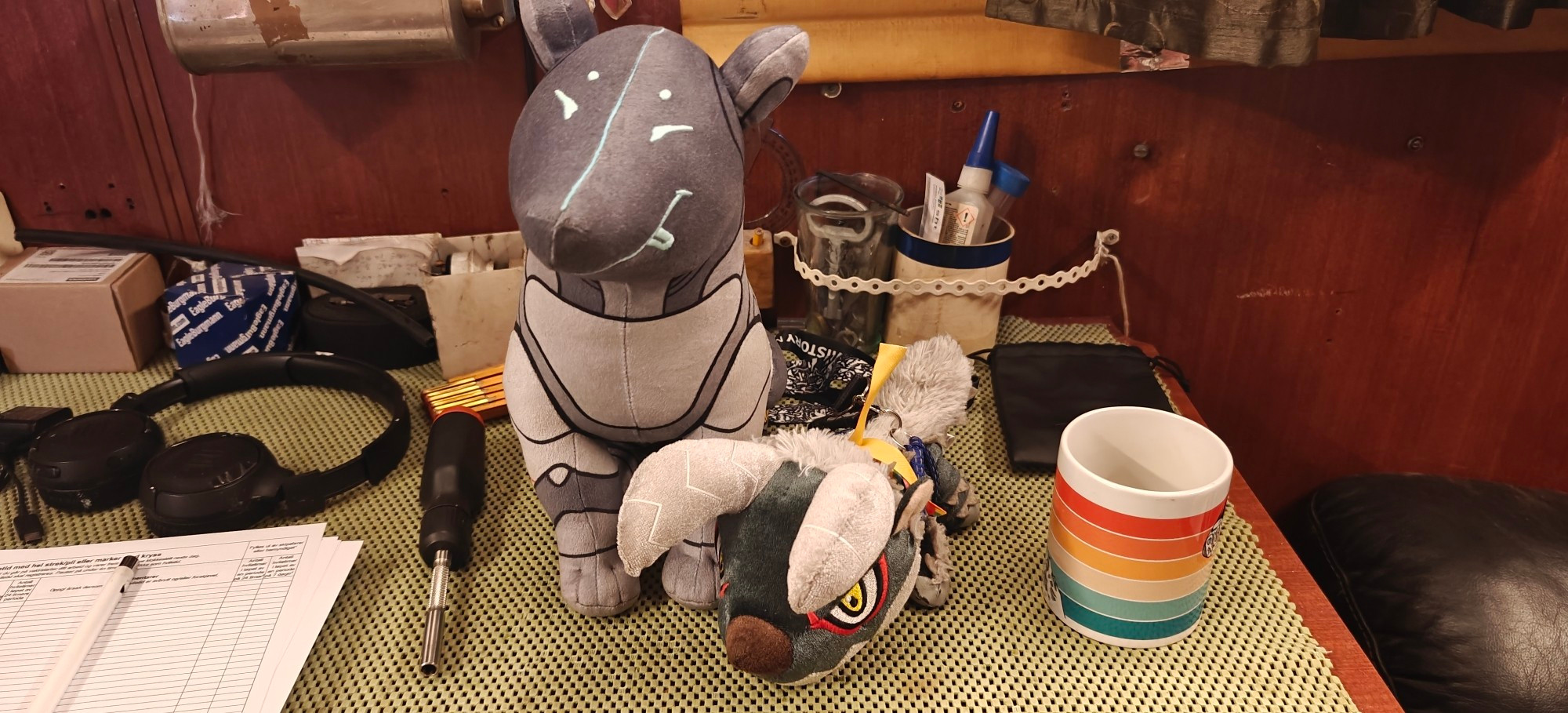 Photo of the Sitting Archie Plushie from Destiny 2, accompanied by the Deformed Stygian Zinogre plushie from Monster Hunter. They're on a desk in a ship cabin