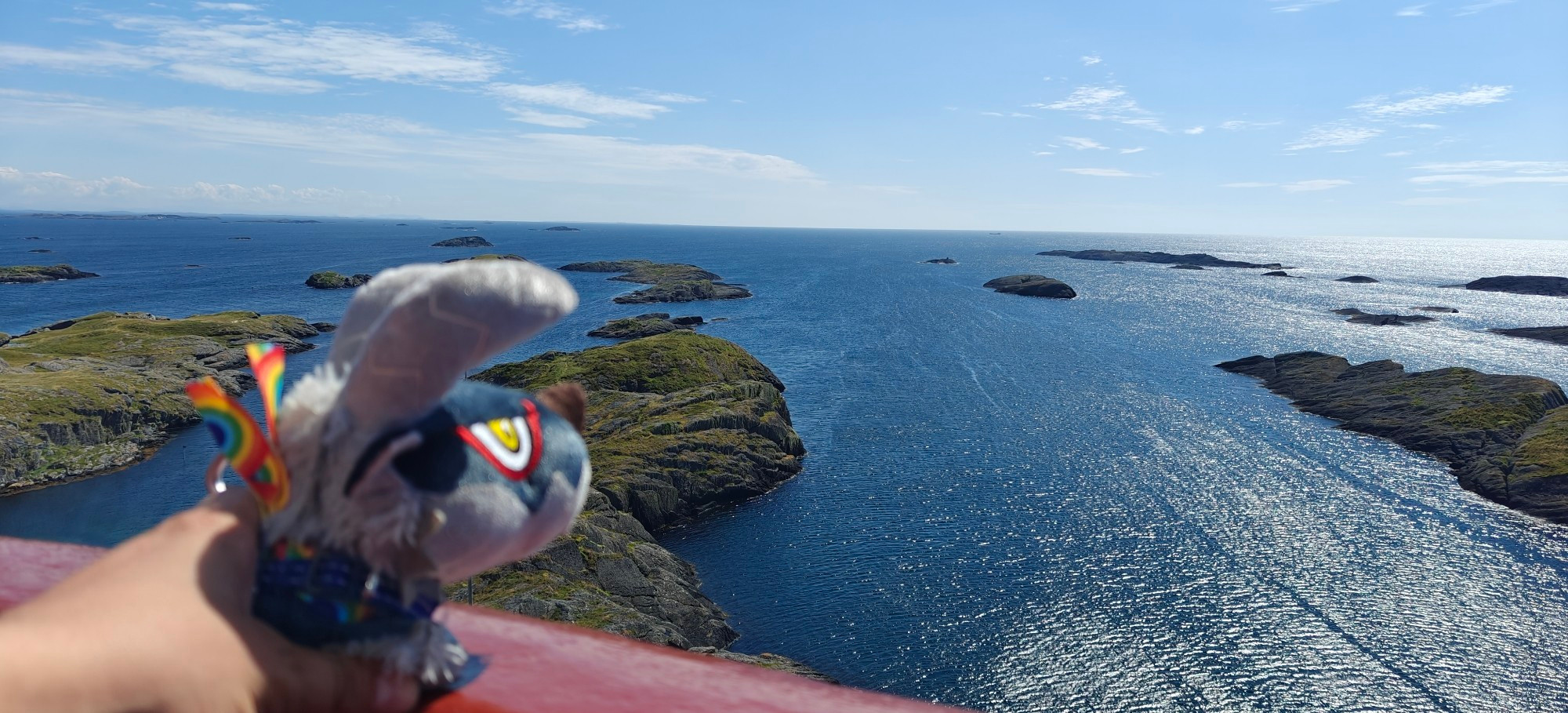 Photo of Deformed Stygian Zinogre plushie looking over a Norwegian coastal area, towards open sea. Photo is taken from atop a lighthouse