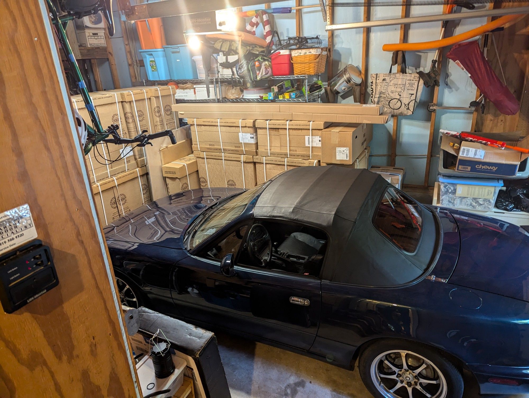 little blue Miata surrounded by boxes and suburban garage crap.