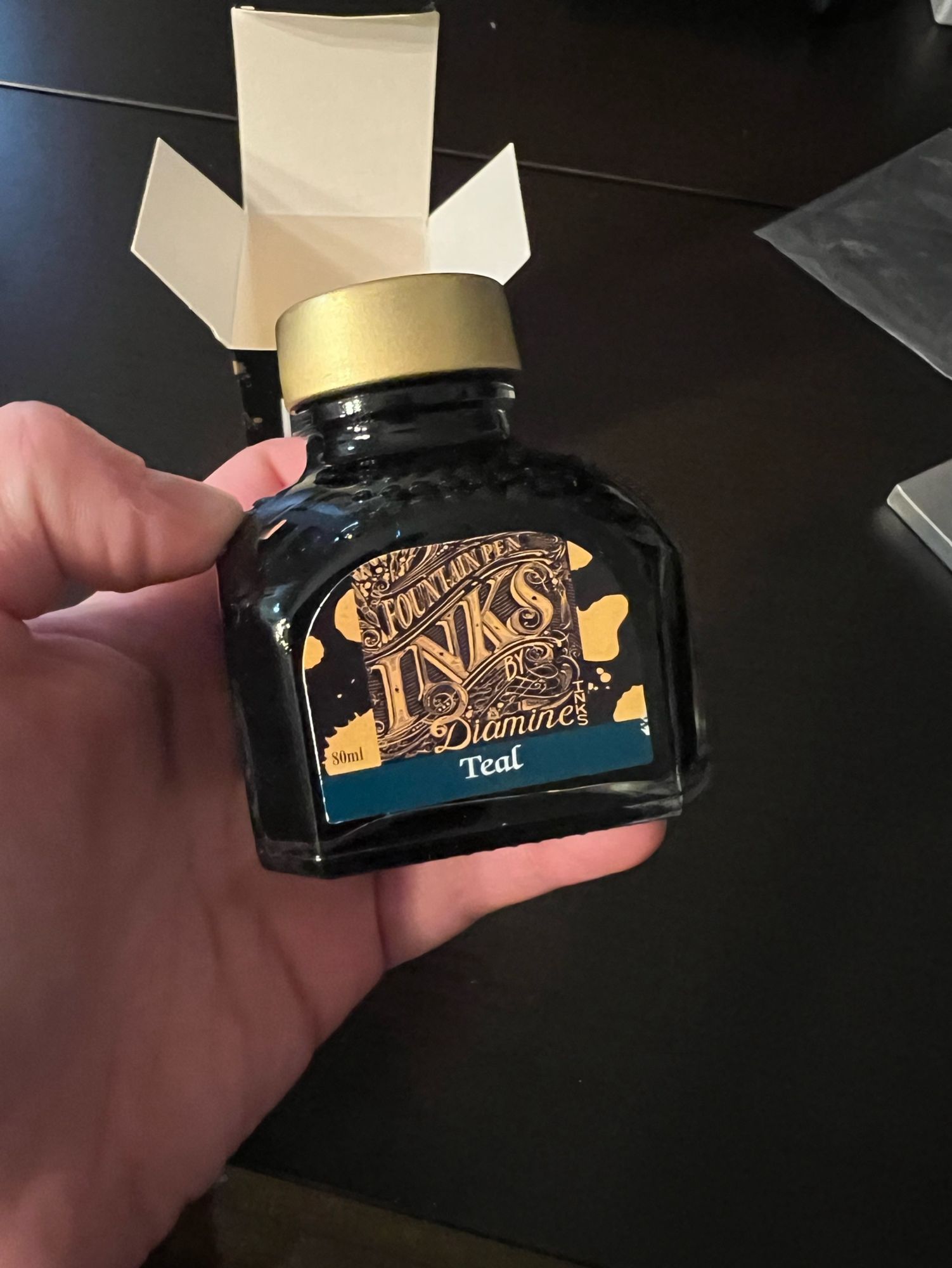 My hand holding a bottle of ink, it reads “Fountain Pen Inks by Diamine” and then, below, “Teal”