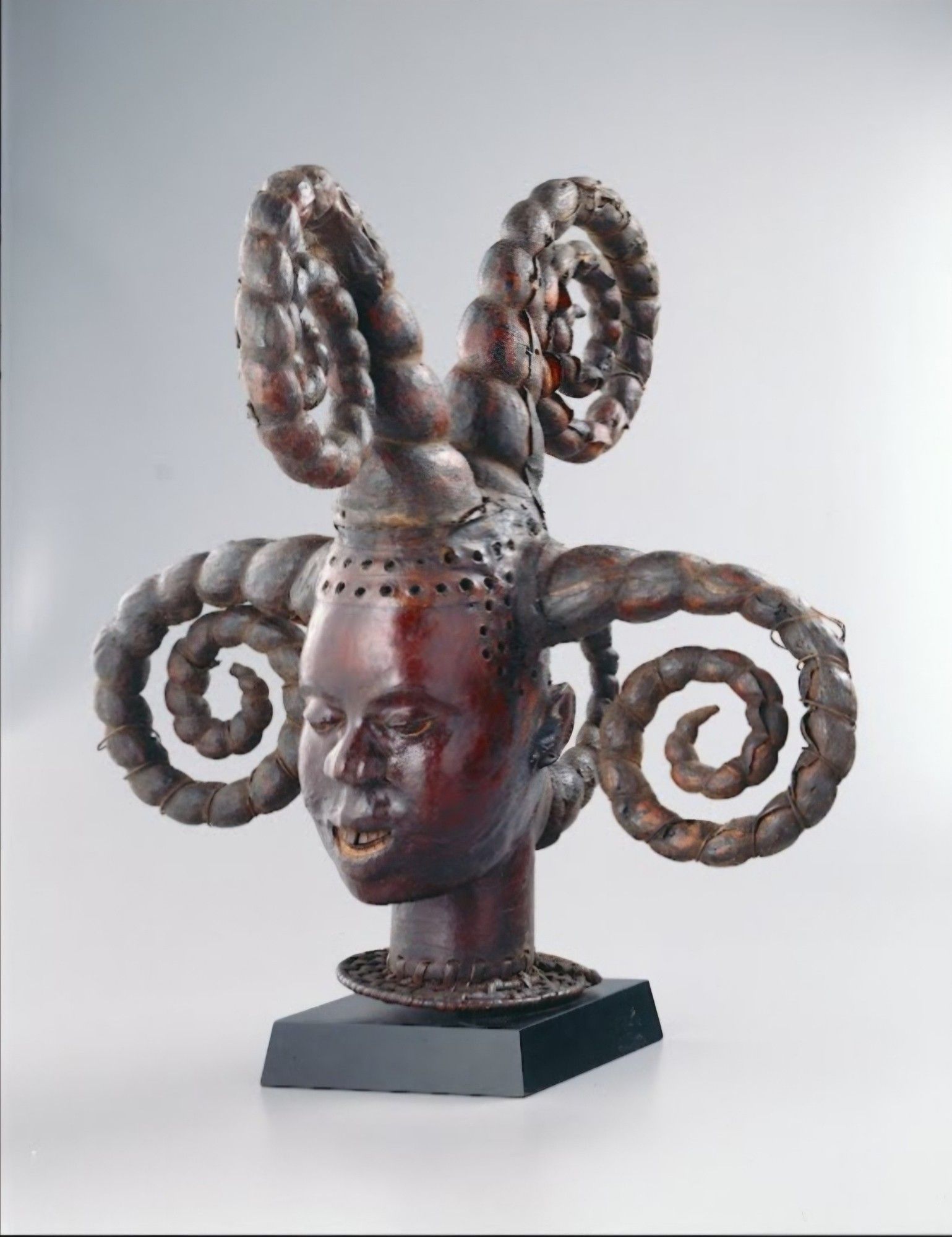 This headdress represents a young woman on the verge of maturity. Adolescent girls in the region wore similar hairstyles at their coming-of-age ceremonies, held after a period of instruction during which they made a ritual transition from childhood to womanhood. The corkscrew style here mimics coiffures produced by weaving extensions of mud and wire into a young woman’s hair. A double line of holes along the hairline formerly held wooden pegs, which represented small tufts of hair that were not swept into the braids. Secured to the top of the performer’s head by a basketry cap, the headdress was worn with a flowing gown that swirled into motion during ikem—a play or dance for venerating ancestors—and at initiations and agricultural rites.