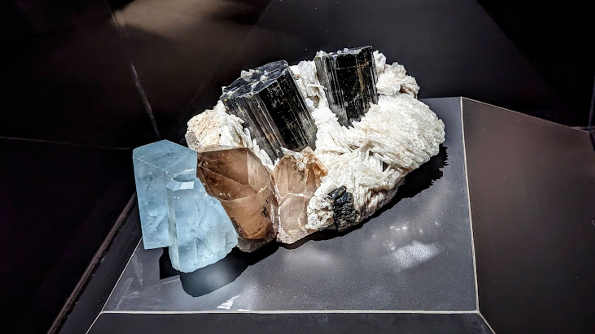 Cluster of minerals including striated elbaite tourmaline, translucent smoky quartz, white albite feldspar, and blue tourmaline.