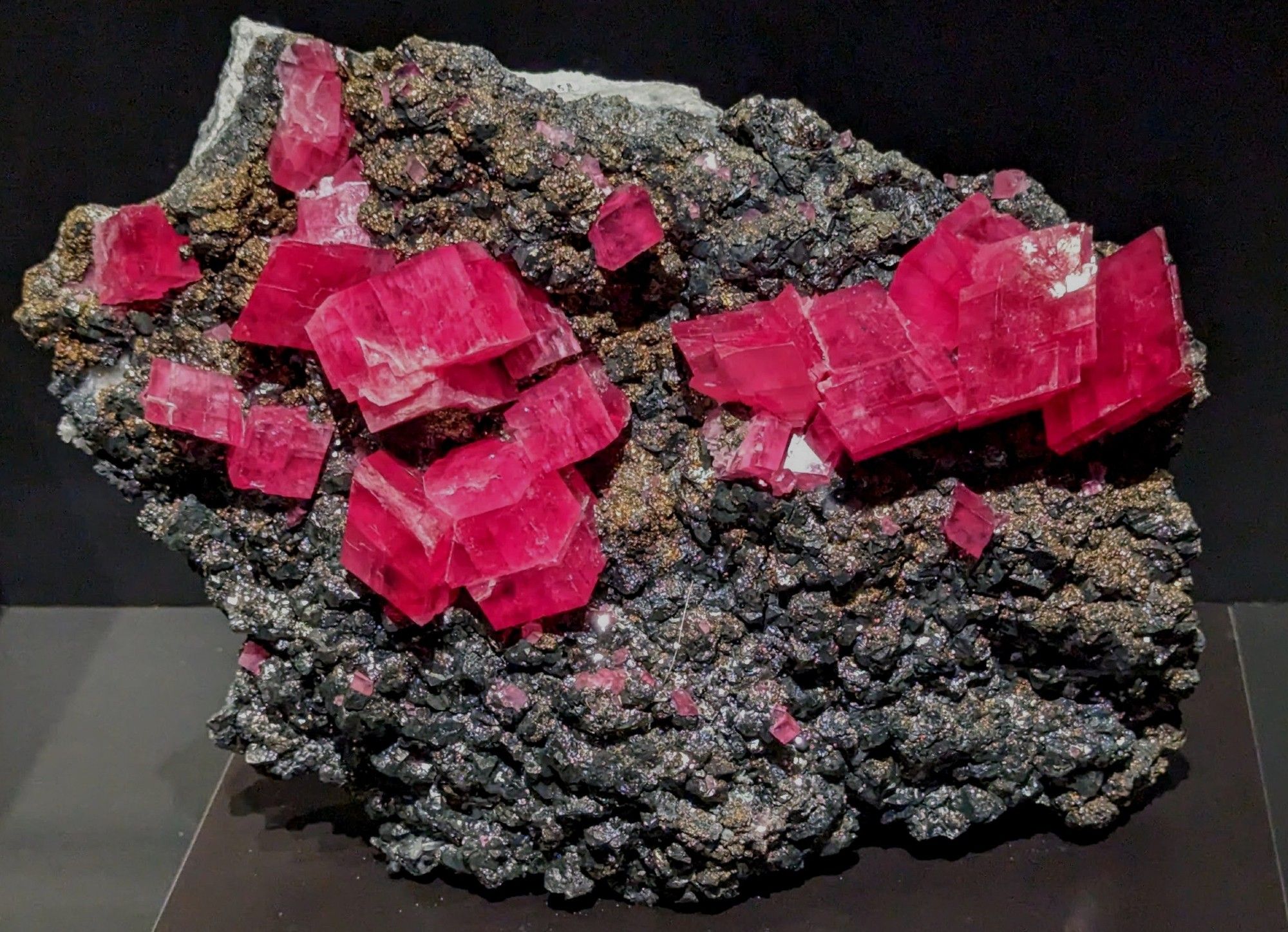 Transparent red rhodochrosite rhombohedra with visible cleavage planes on black tetrahedrite.