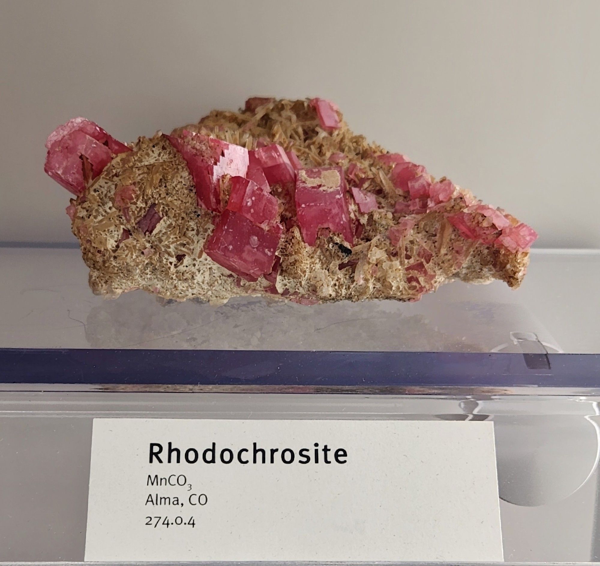 Translucent pink rhodochrosite rhombohedrons on unnamed tan crystalline matrix. 

Label reads:
Rhodochrosite
MnCO3
Alma, CO
274.0.4