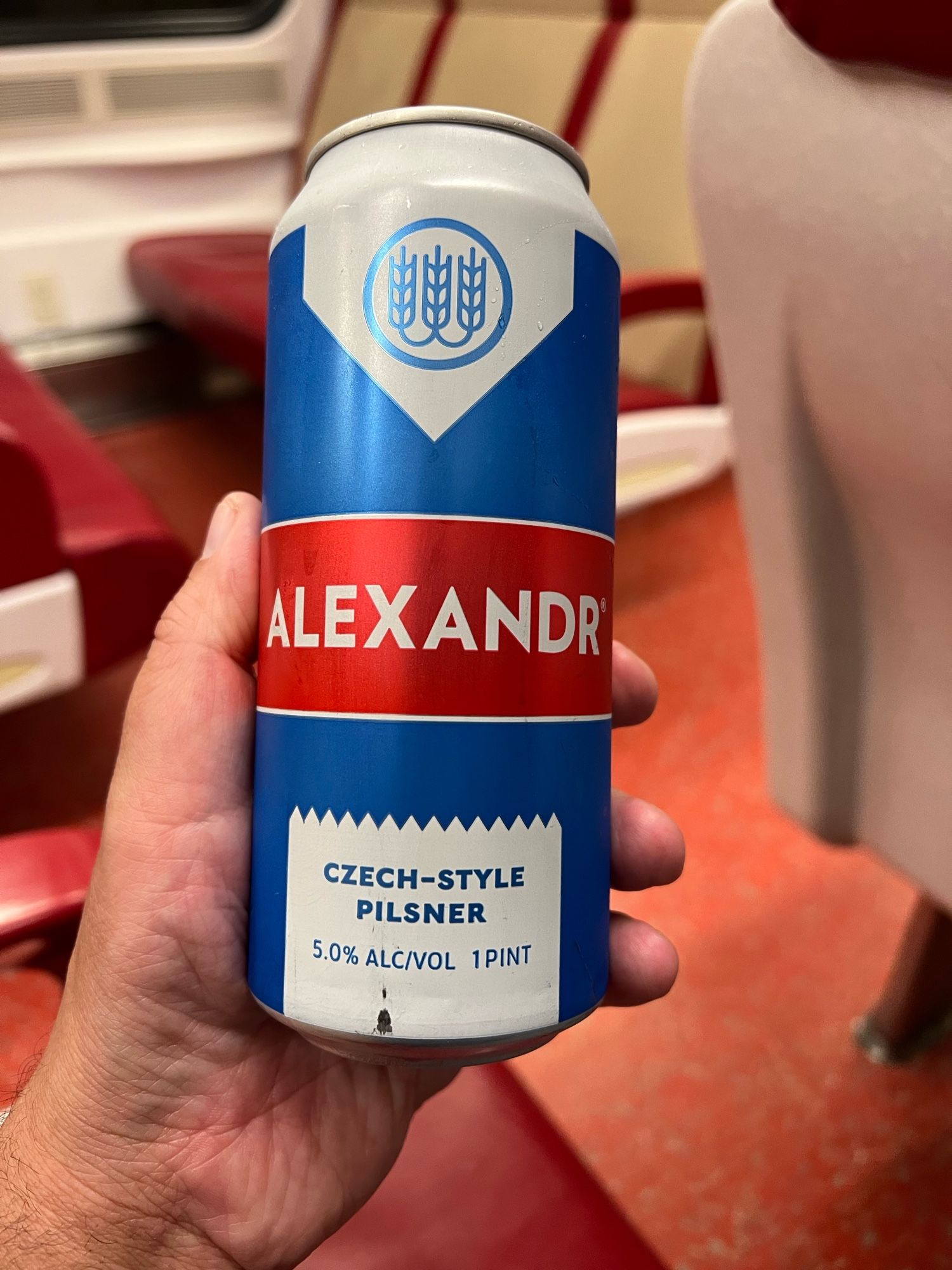 A can of Schilling Beer Co. Alexandr in my hand with train seats in the background