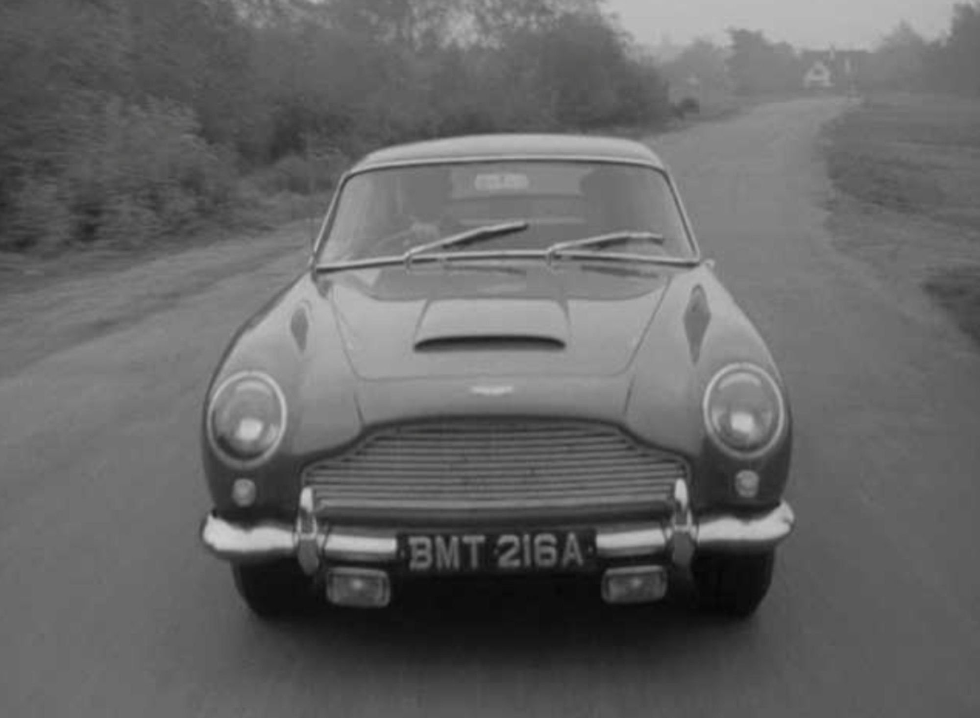 Screenshot aus "Simon Templar". Der Aston Martin DB5, hier noch in Dubonnet Red lackiert, mit dem aus James Bond bekannten Kennzeichen BMT 216A. Das Fahrzeug war der allererste Prototyp des DB5. Für James Bond wurde das Fahrzeug umgebaut und in Silber umlackiert.