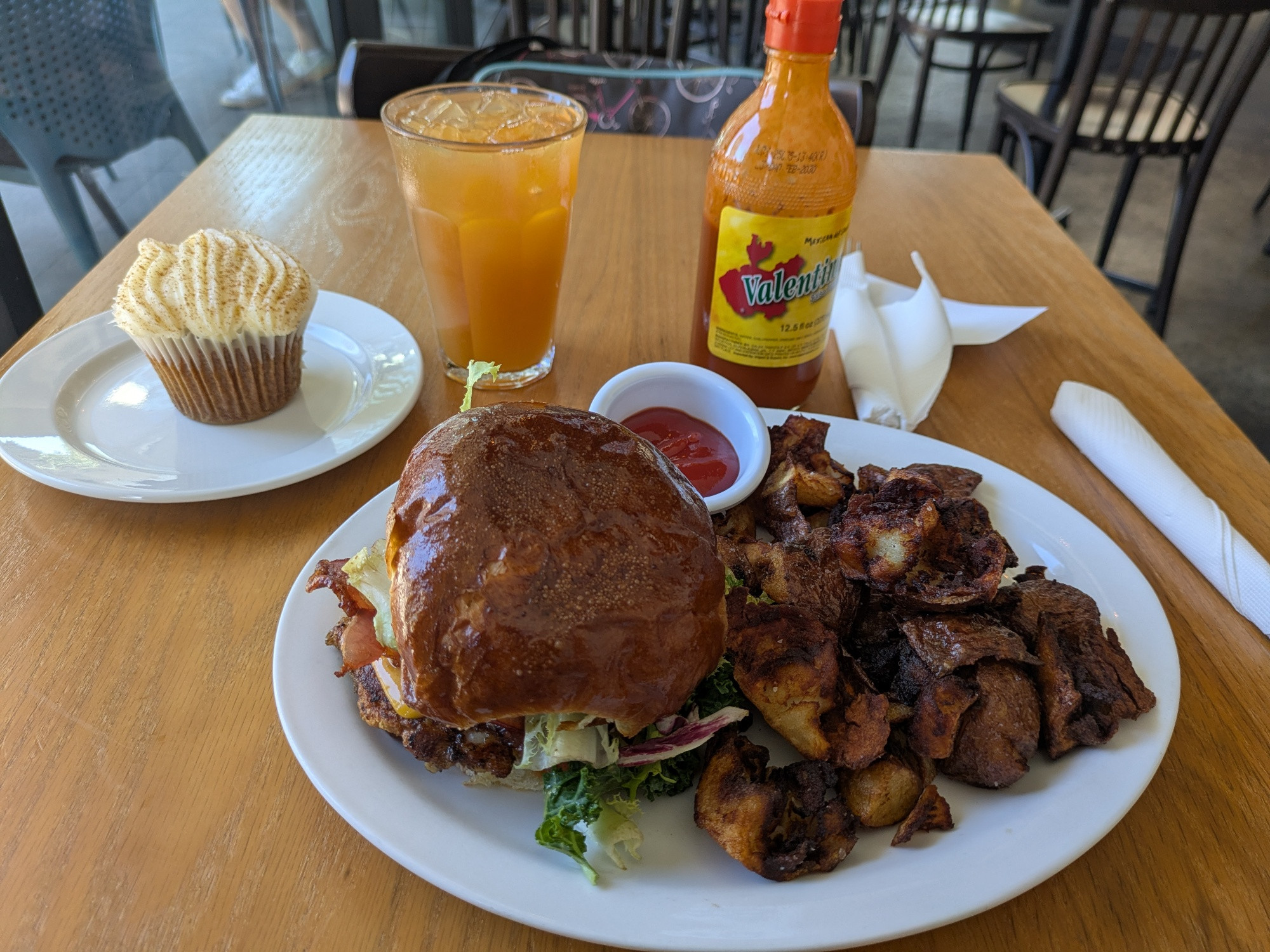 a club sandwich and crispy fried potatoes on a white plate, also a cupcake on a separate plate and a glass of iced tea