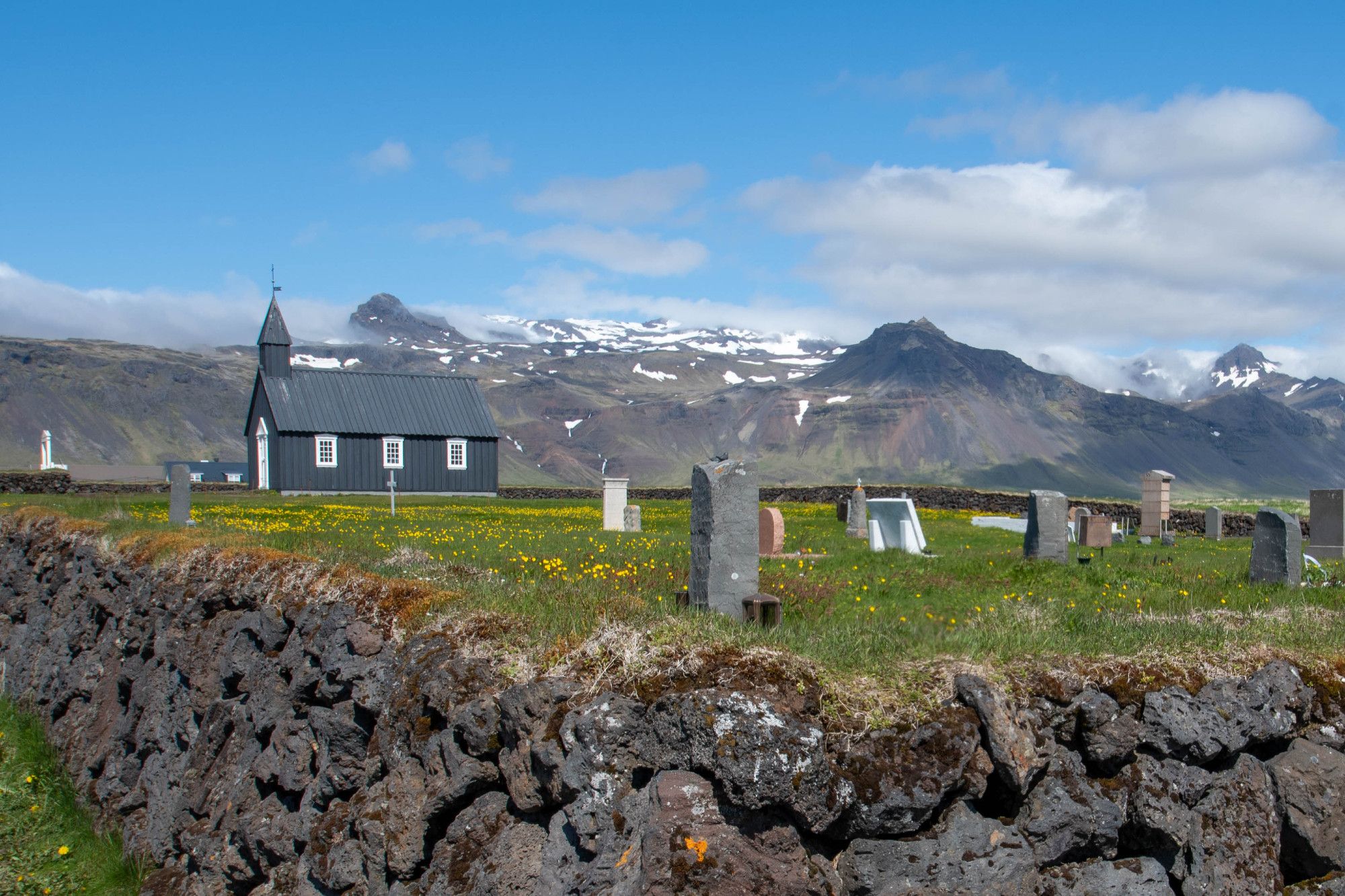 Black church in churchyard with snowy mountains