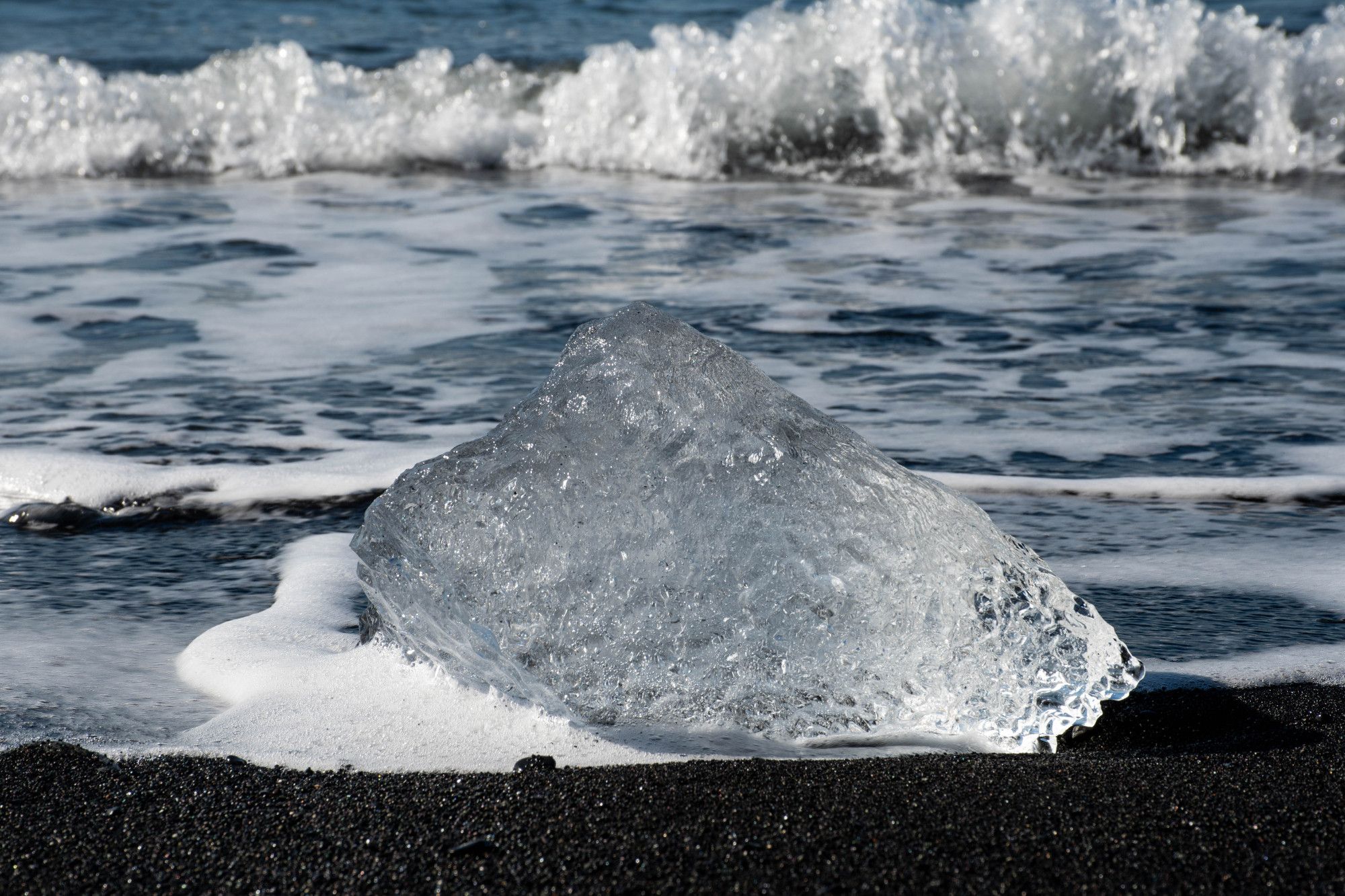 Block of ice from a glacier on a black sand beach with waves crashing from the sea