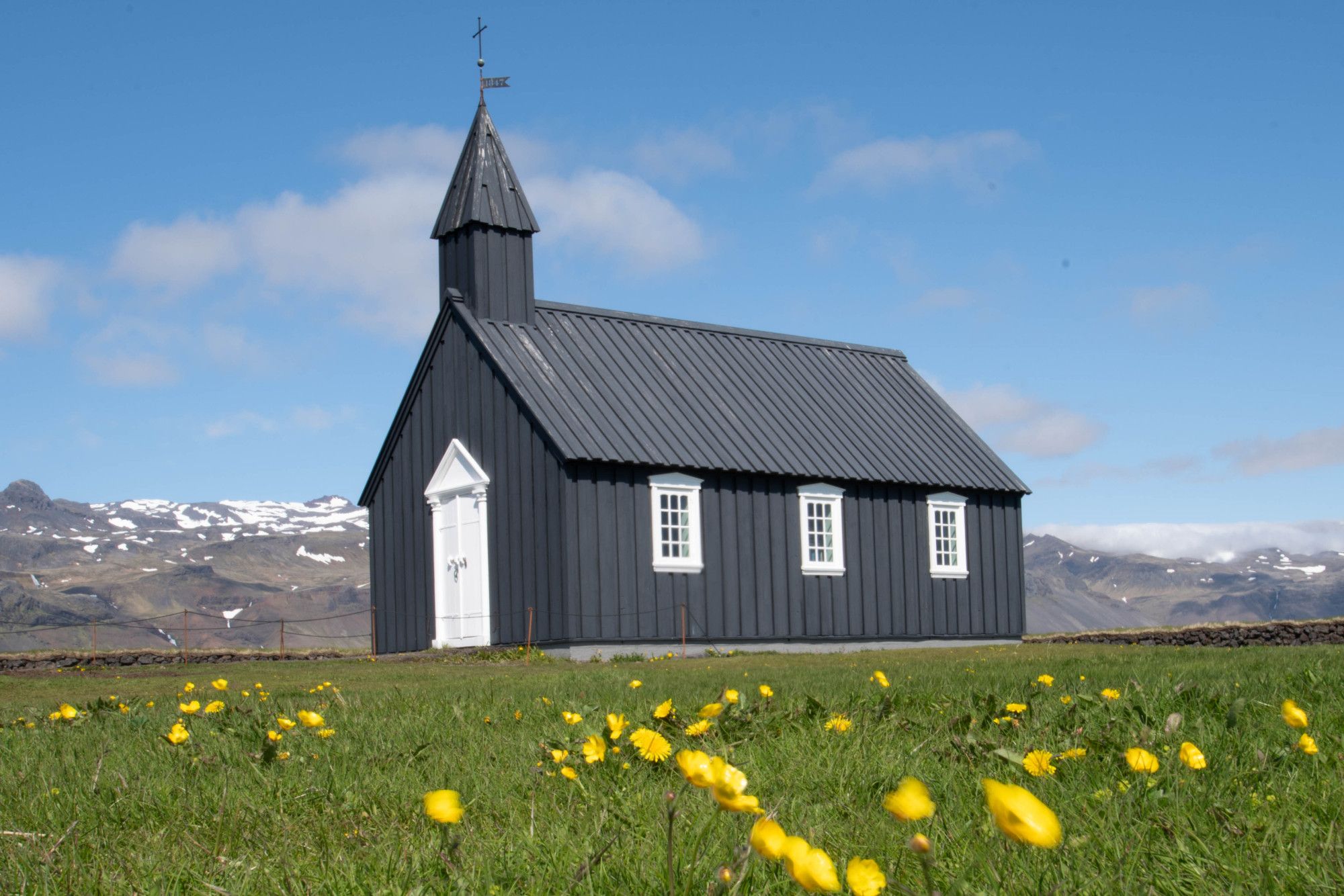 Black church in buttercupas with snowy mountains