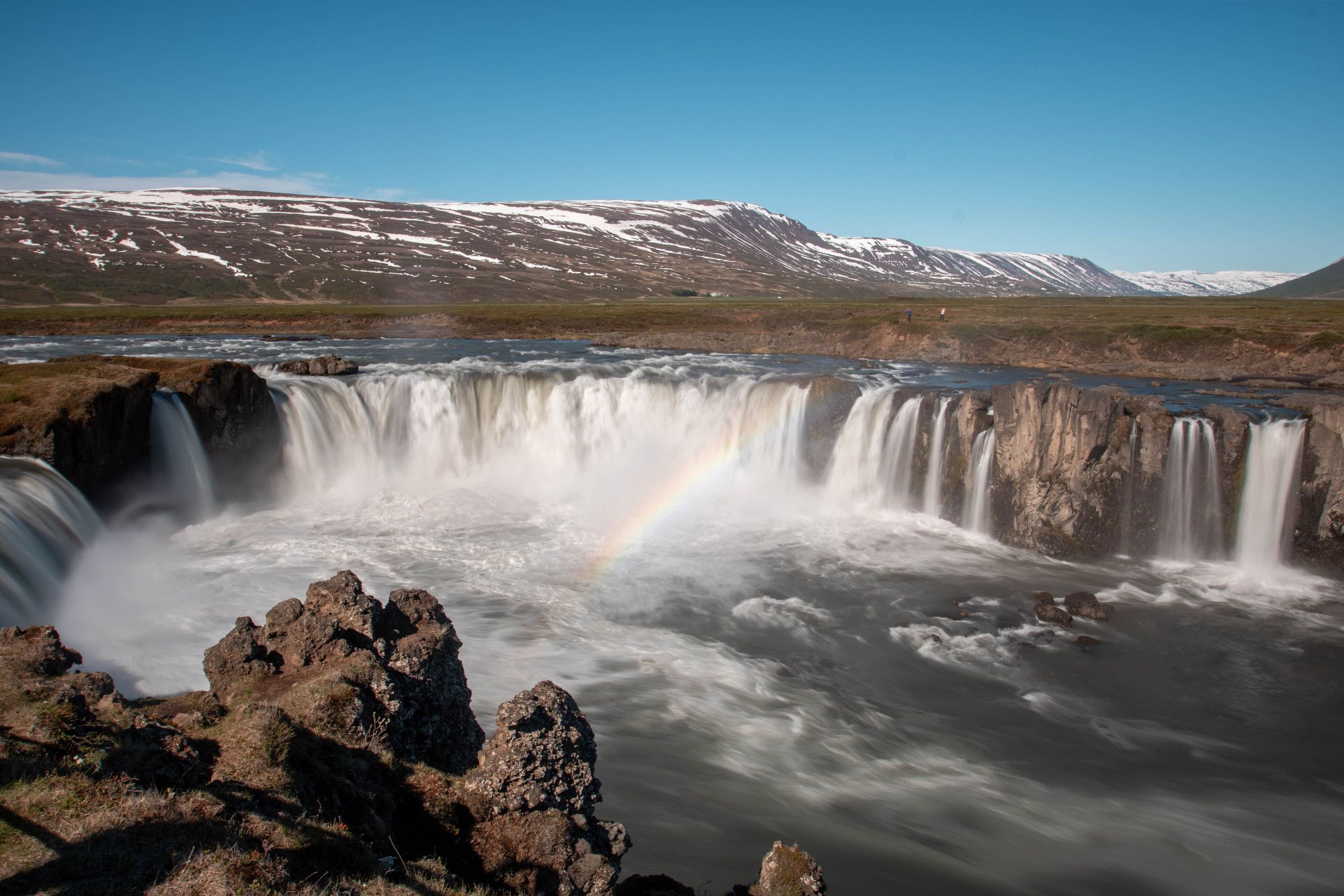 Large horseshoe shape waterfall with rainbow. snowy mountains behind