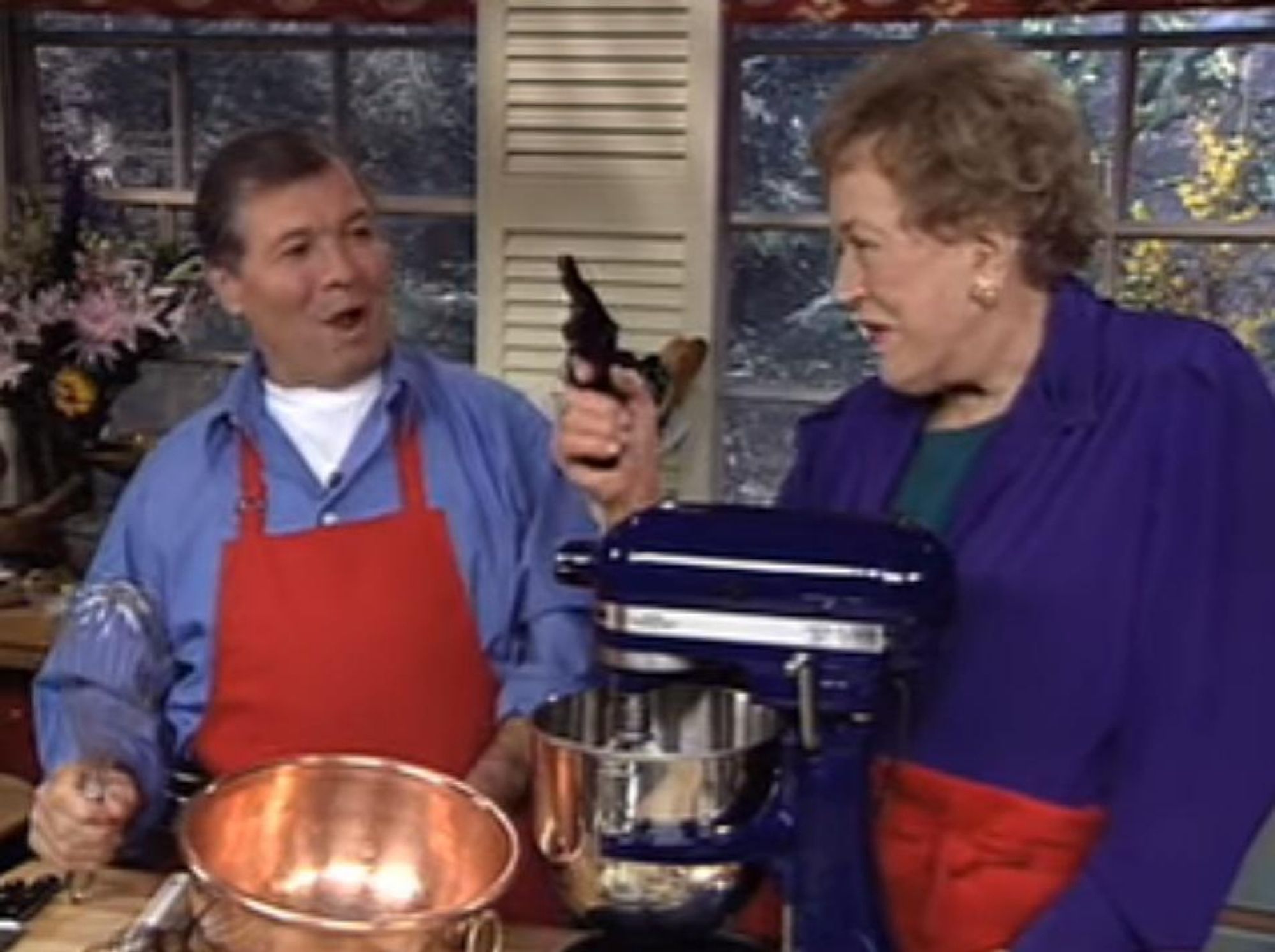 jacques pepin and julia child. julia child is holding a revolver while jacques pepin looks surprised but excited