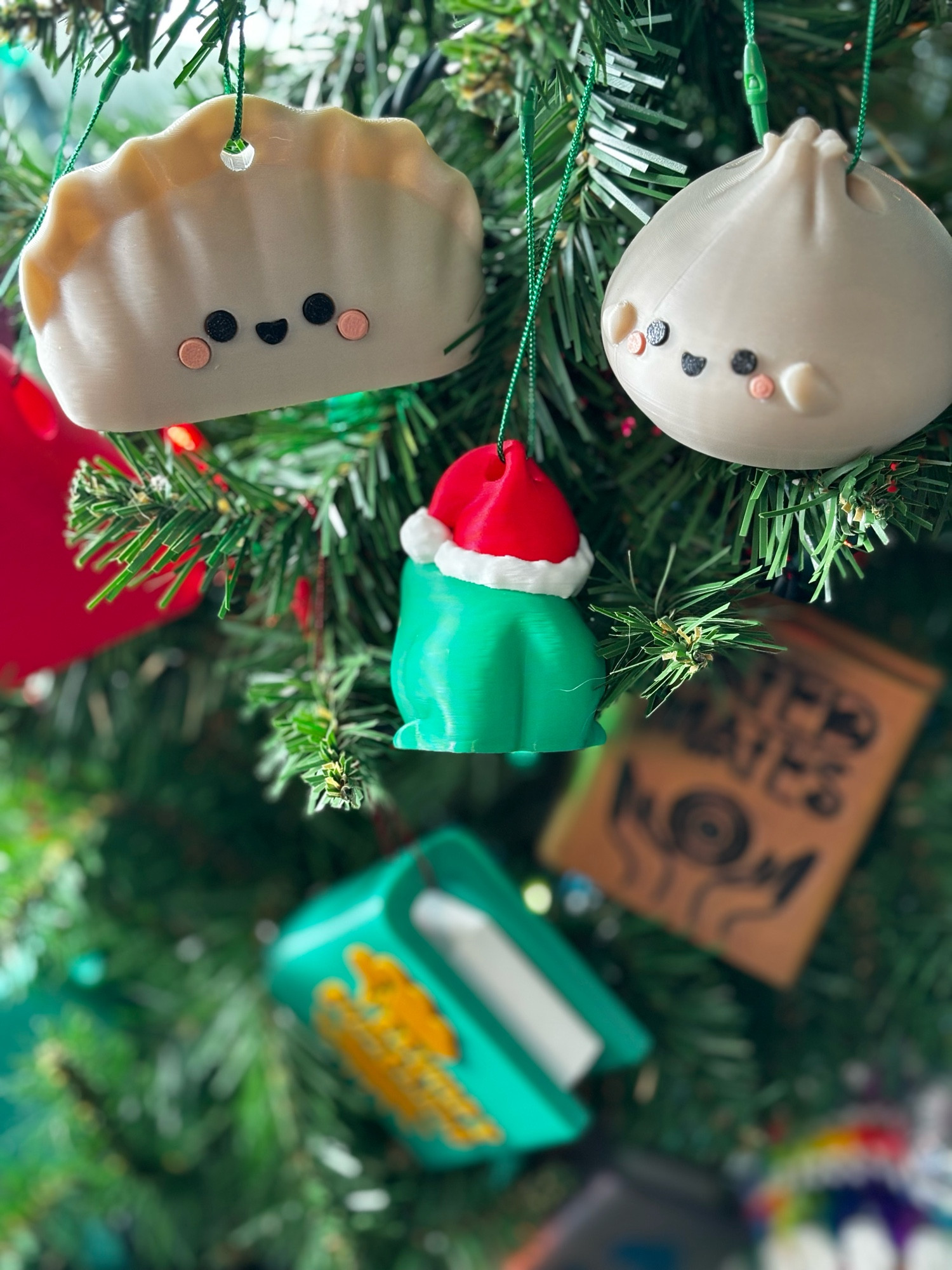 A small 3d printed green frog wearing a Santa hat, hung on a Christmas tree. It is turned to show that it has a butt on the back