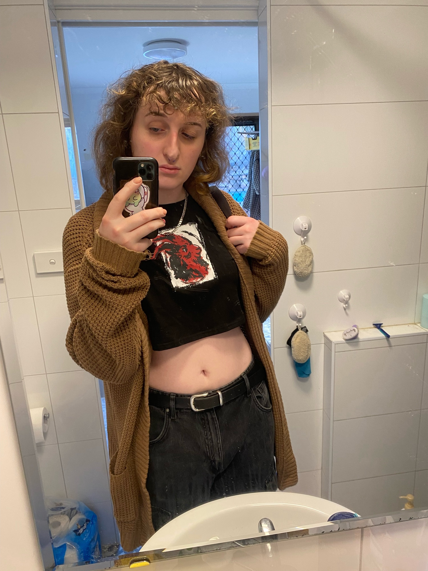 mirror selfie of cassie wearing a black crop top, black jeans and a brown cardigan