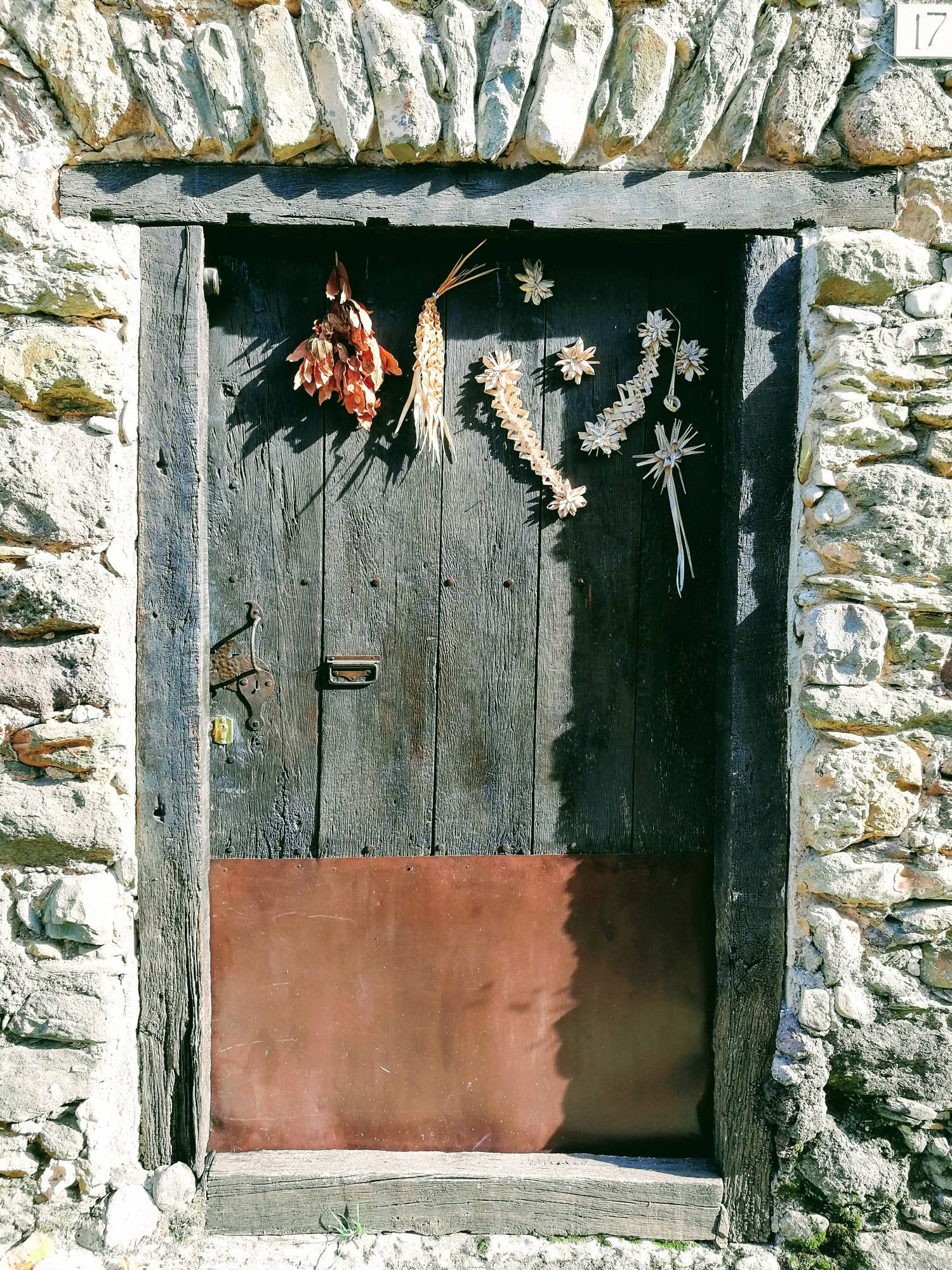 Small greyed wooden door with metal sheet repair at the bottom and dried corn doilies