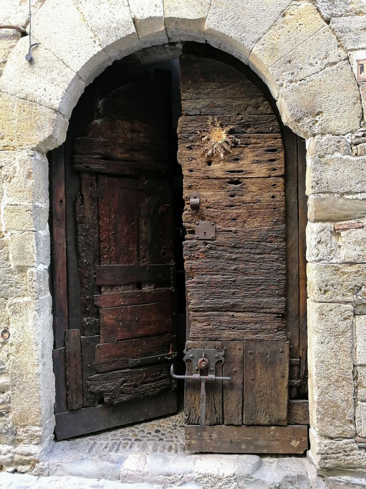 In an arched stone frame, very old wooden double door slightly ajar, with a dried cardabelle nailed to it - reputed to bring good luck.