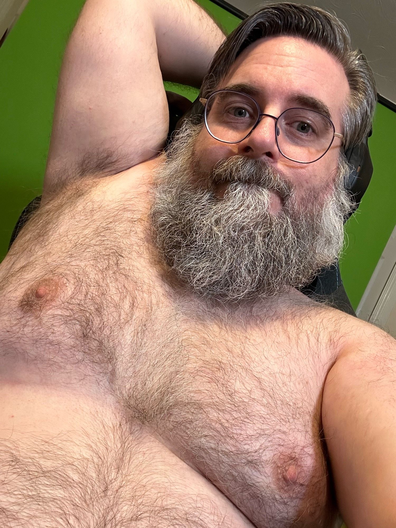 Me, a greying-haired and grey-bearded white man with glasses, seated shirtless in front of a green screen in the background, showing my hairy chest and part of my hairy belly, and with my right arm raised behind my head displaying my hairy armpit