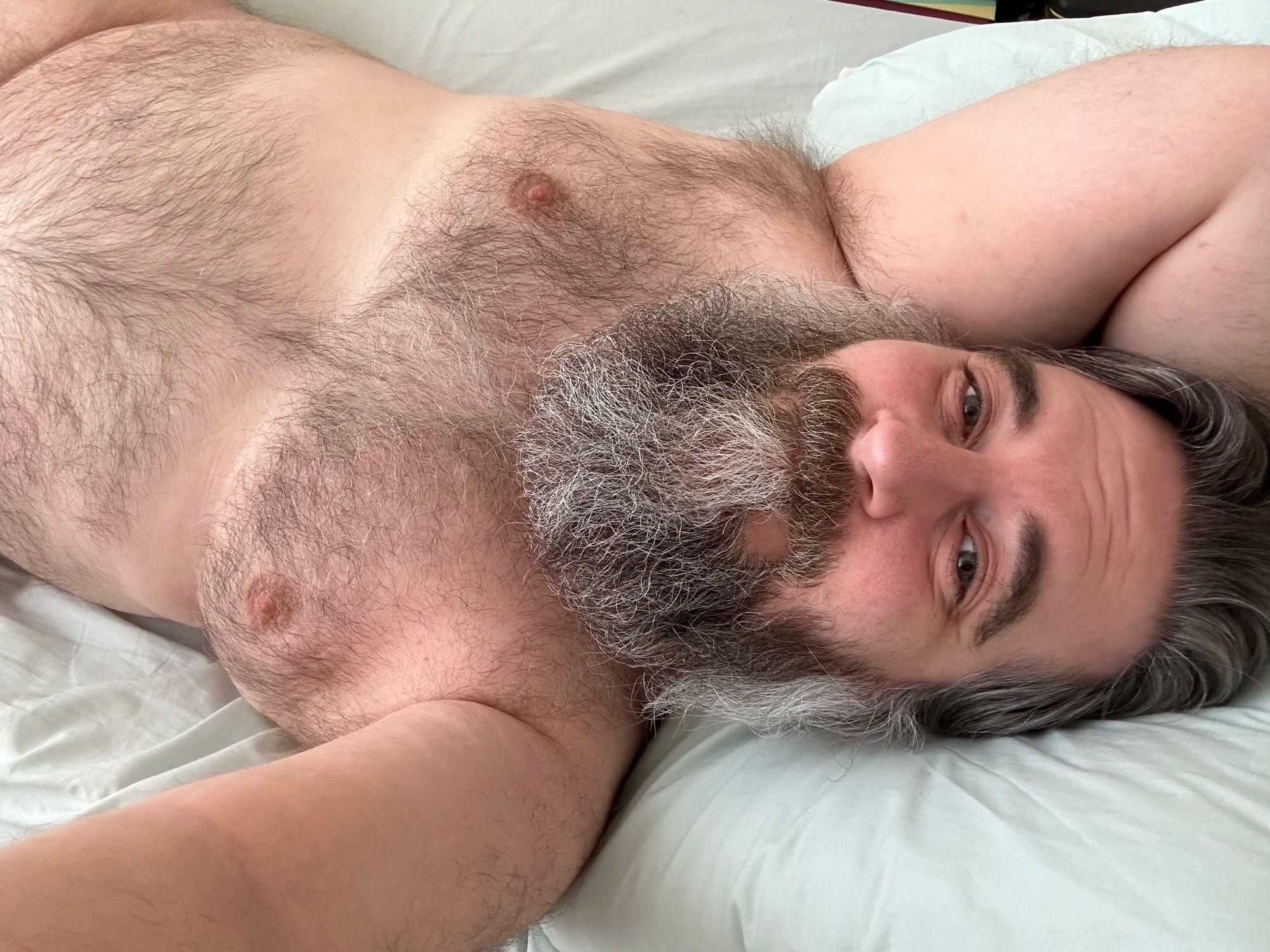 Me lying in bed, showing my hairy belly, chest, armpit and bearded face and looking snuggly