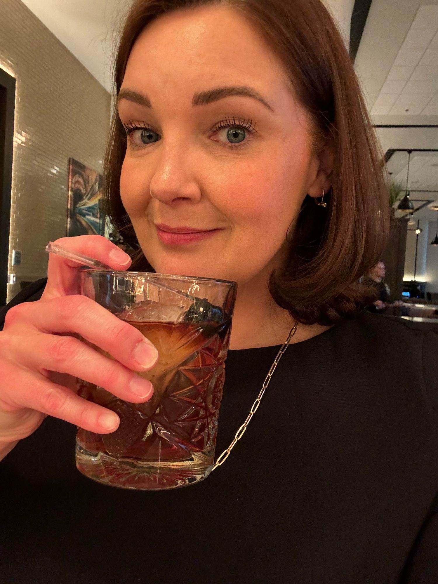 A lady wearing her most “tell me you’re in house counsel for a financial services company without telling me” getup with a smoked manhattan in hand at a hotel bar