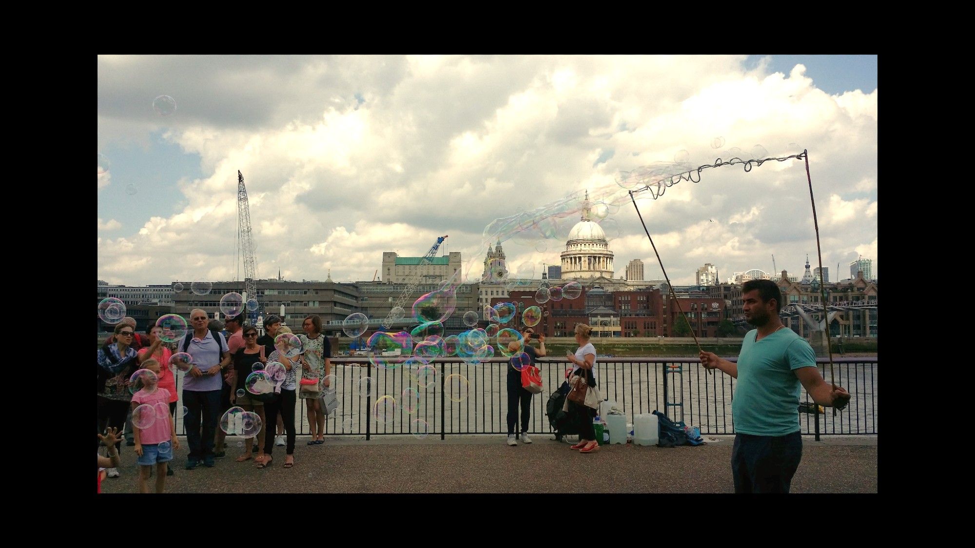 Street scene, London

A vendor blows iridescent bubbles on the banks of the Thames while delighted passers by watch.