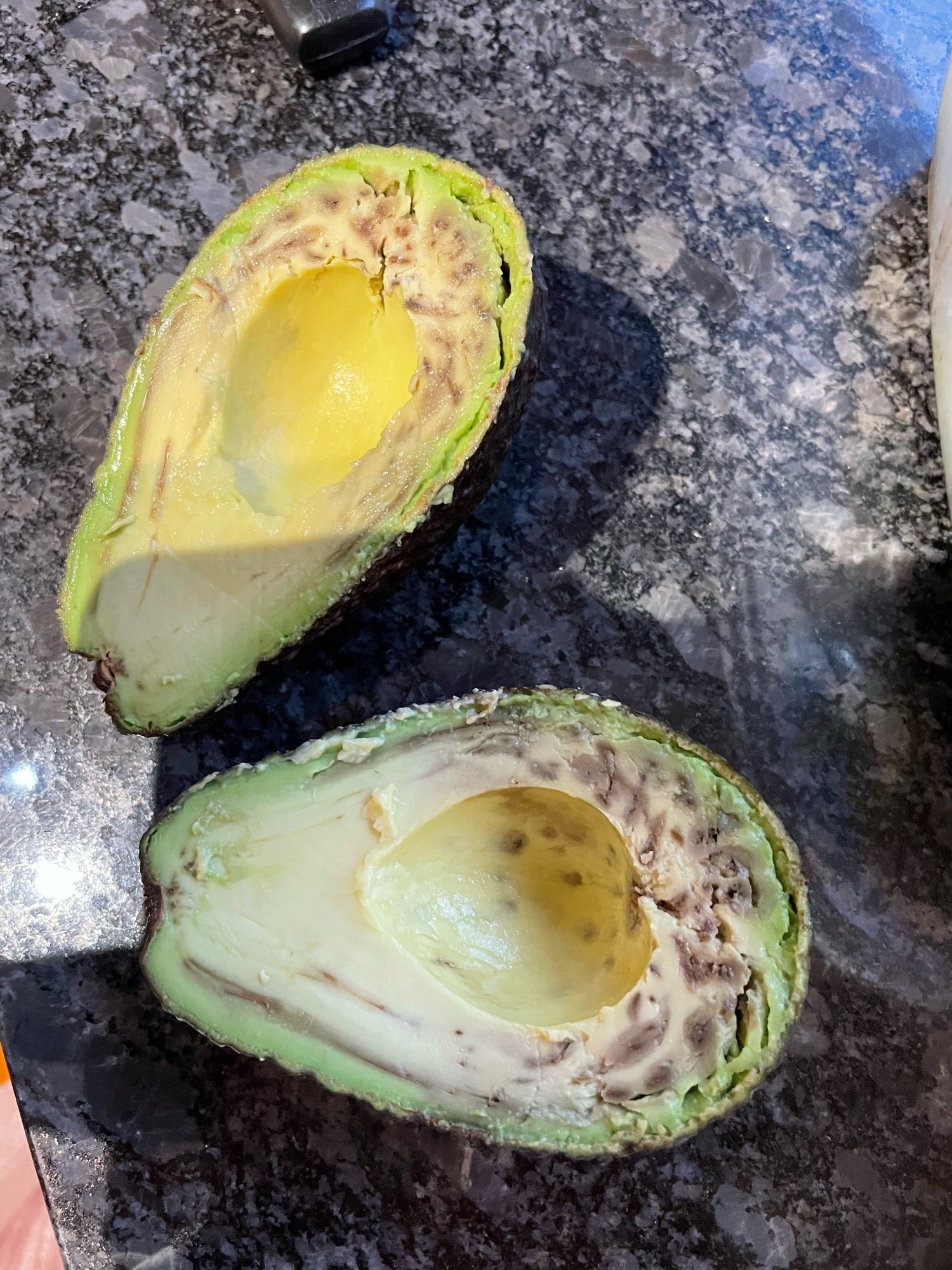 An avocado cut open to reveal black spots through most of the flesh