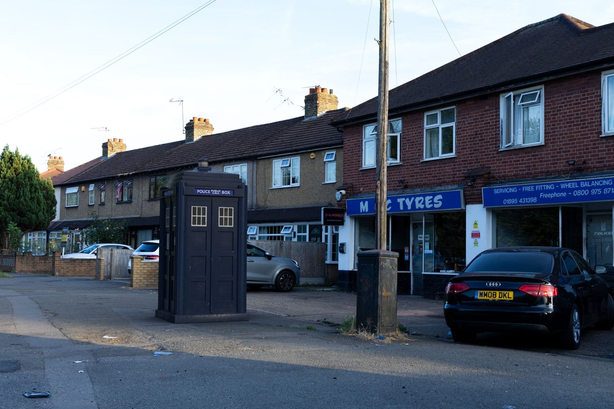 A 3D composite of a police box in front of houses and to the left of a telegraph pole.