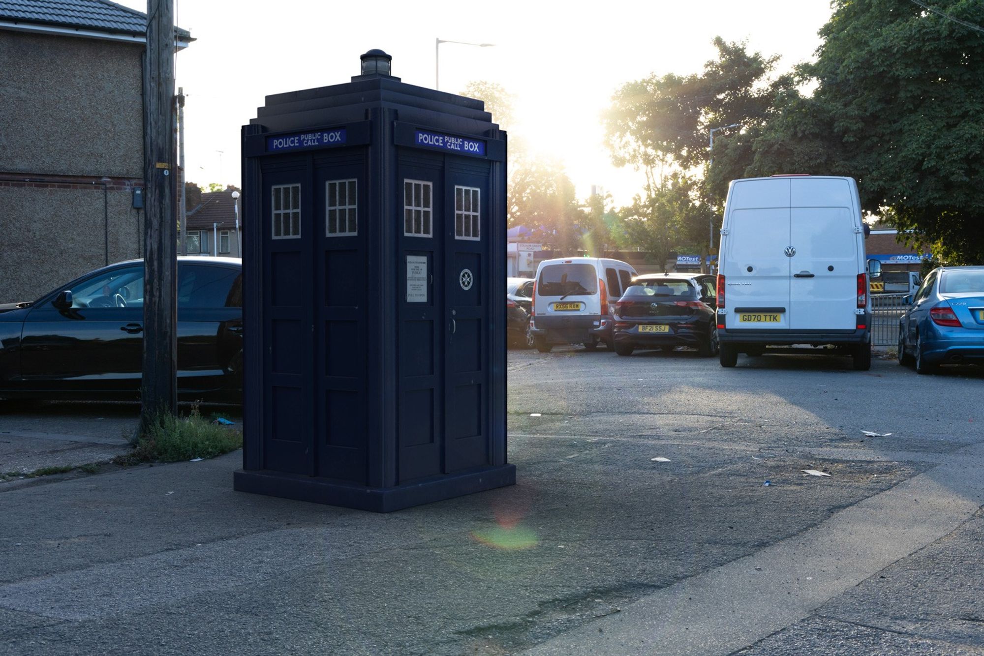 A 3D composite of a police box on a pavement with the setting sun behind it