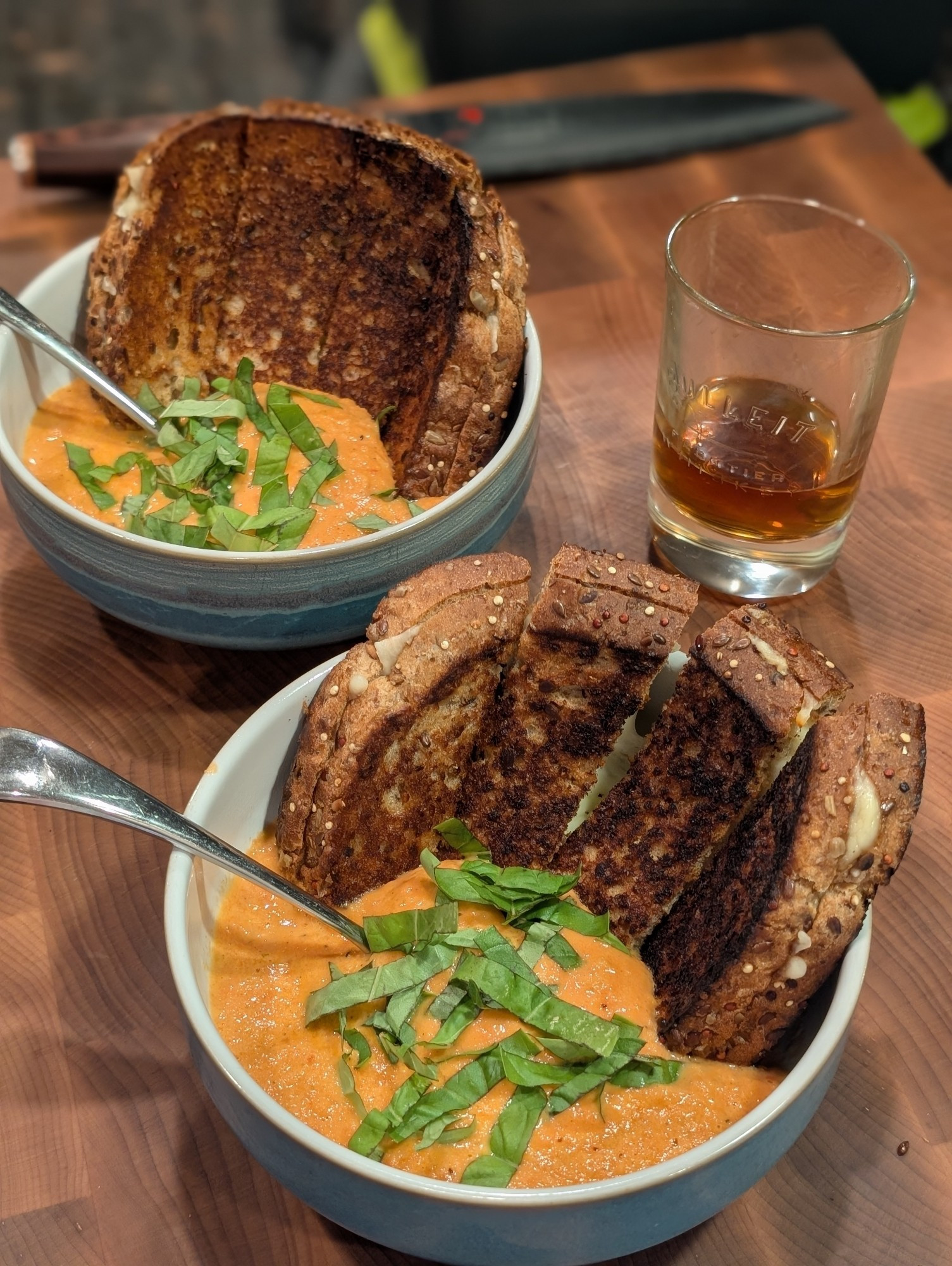 Two bowls of a bright orange creamy tomato soup (lightened with heavy cream), with a sprinkling of sliced basil. Dunked into each  soup is a grilled cheese sliced into fingers.