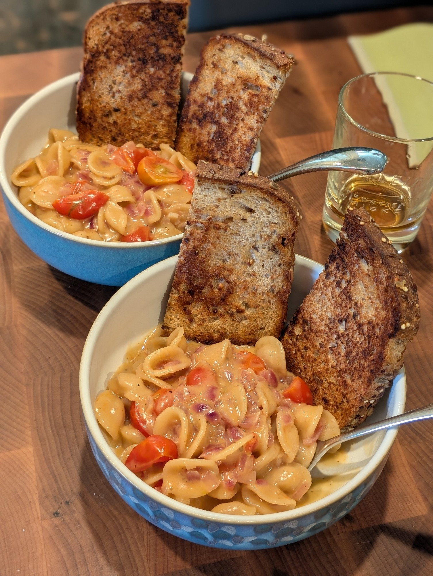 Two bowls of a cheesy, saucy shell pasta with tomatoes, and some griddled toast on the side.