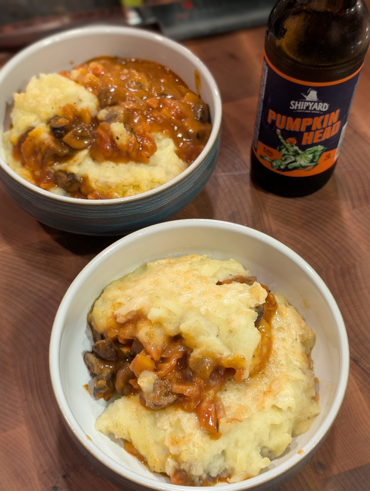 Two servings of the pie dished up into bowls, with a pumpkin beer sitting next to them.