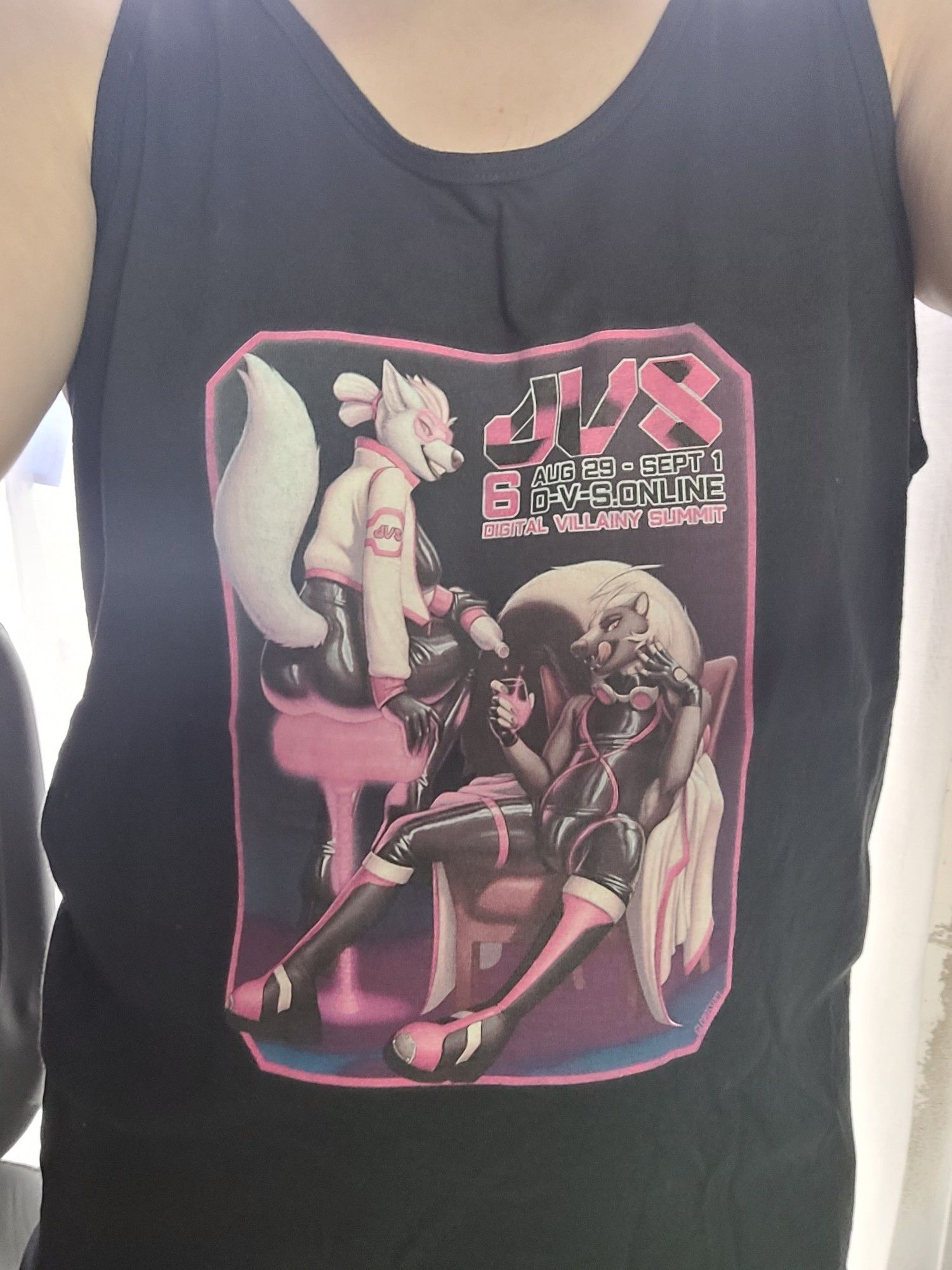 A woman's torso wearing a loose black tanktop with art printed on it. The art shows two anthropomorphic characters, both dressed mostly in black latex with pink accents. One of them is reclining in an armchair as the other pours them a drink. Above them is some text in black and pink: DVS 6, Digital Villainy Summit, Aug 29 to Sept 1, D-V-S.online