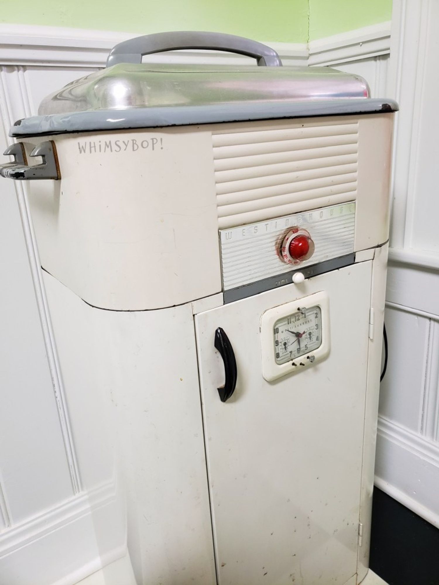 Westinghouse warmer cabinet. It's an electrified, floor-standing combination of a waterbath (top, aluminum dome with bakelite handle)warmer cabinet (bottom, vertical bakelite arch handle. Clock face for timing. Dial made of clear lucite/glass with a red dome visible inside.