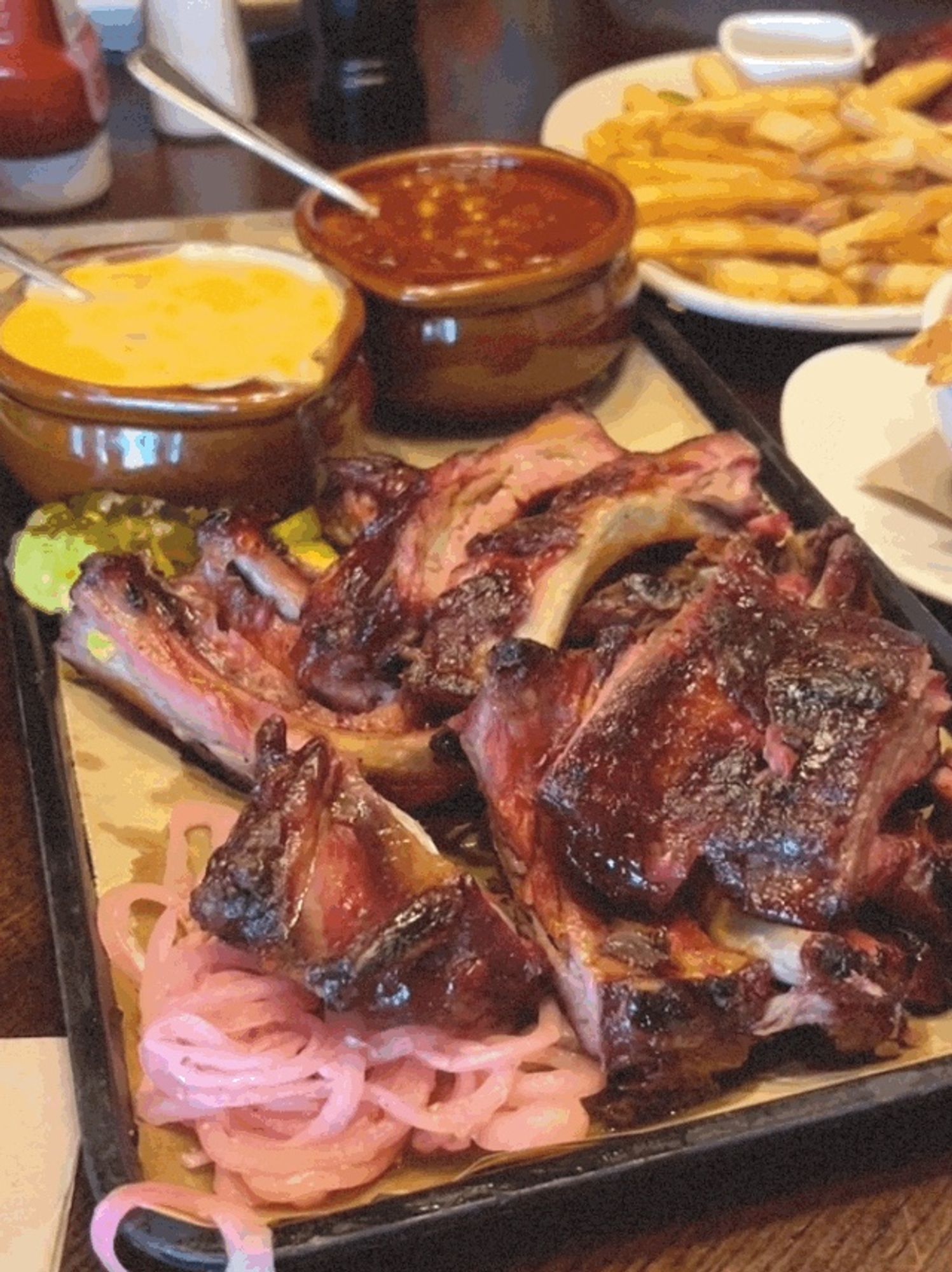 Cut pork baby back ribs glistening in the light on a serving plate with a bowl of cheesy corn and a bowl of bbq baked beans.