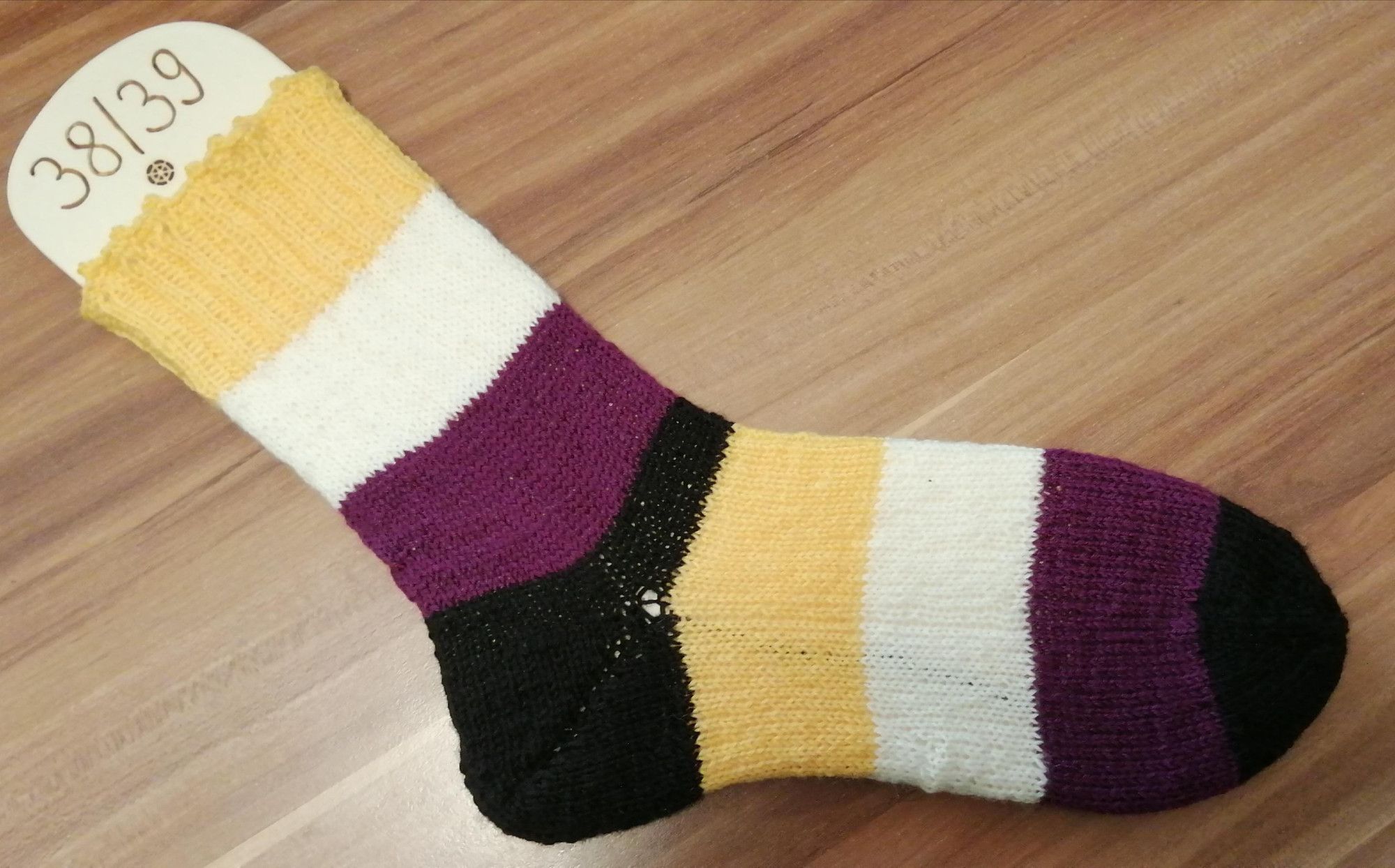 knitted sock in the enby flag collors